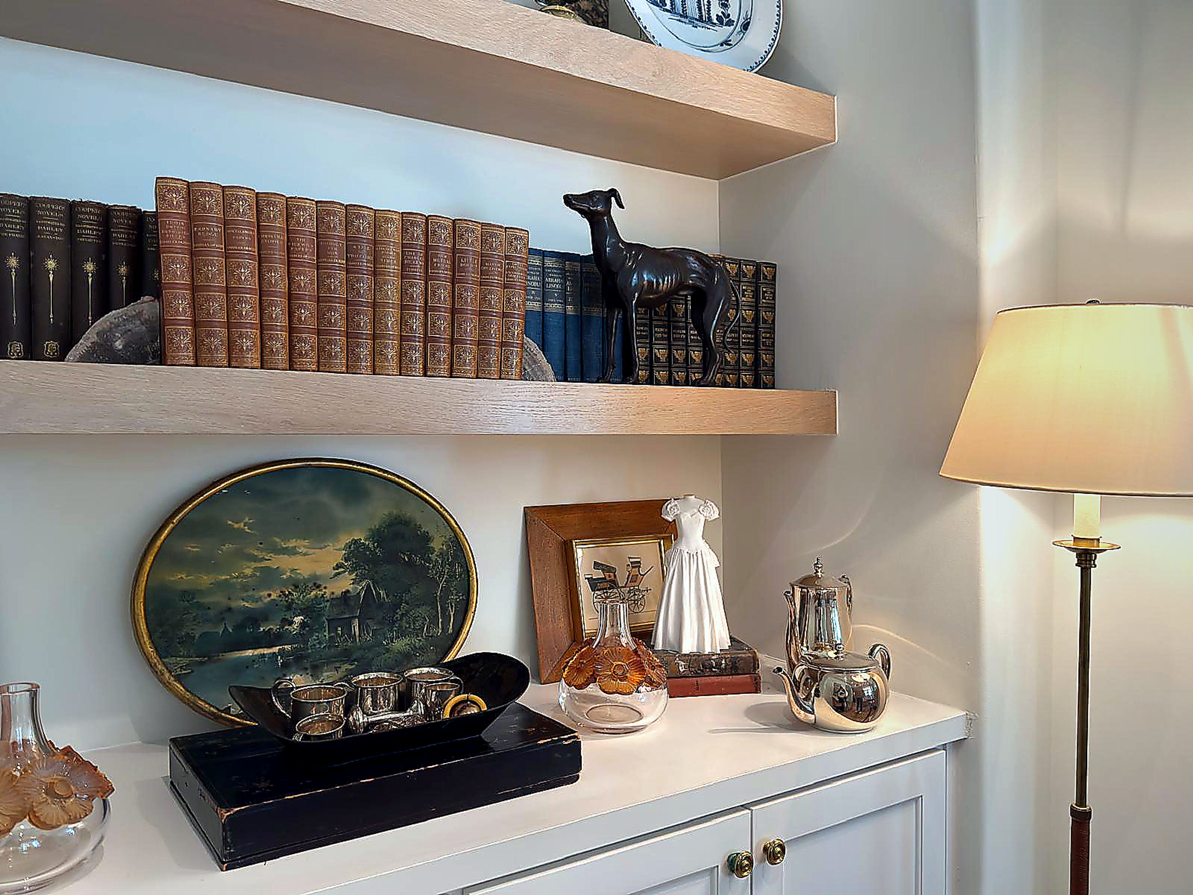 White wedding gown sculpture displayed on a bookshelf among books, decorative objects, and framed artwork.