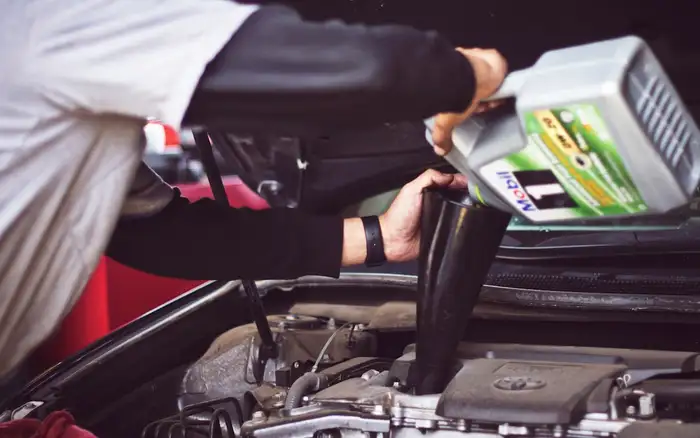 A mechanic servicing fluids under the open hood of a car