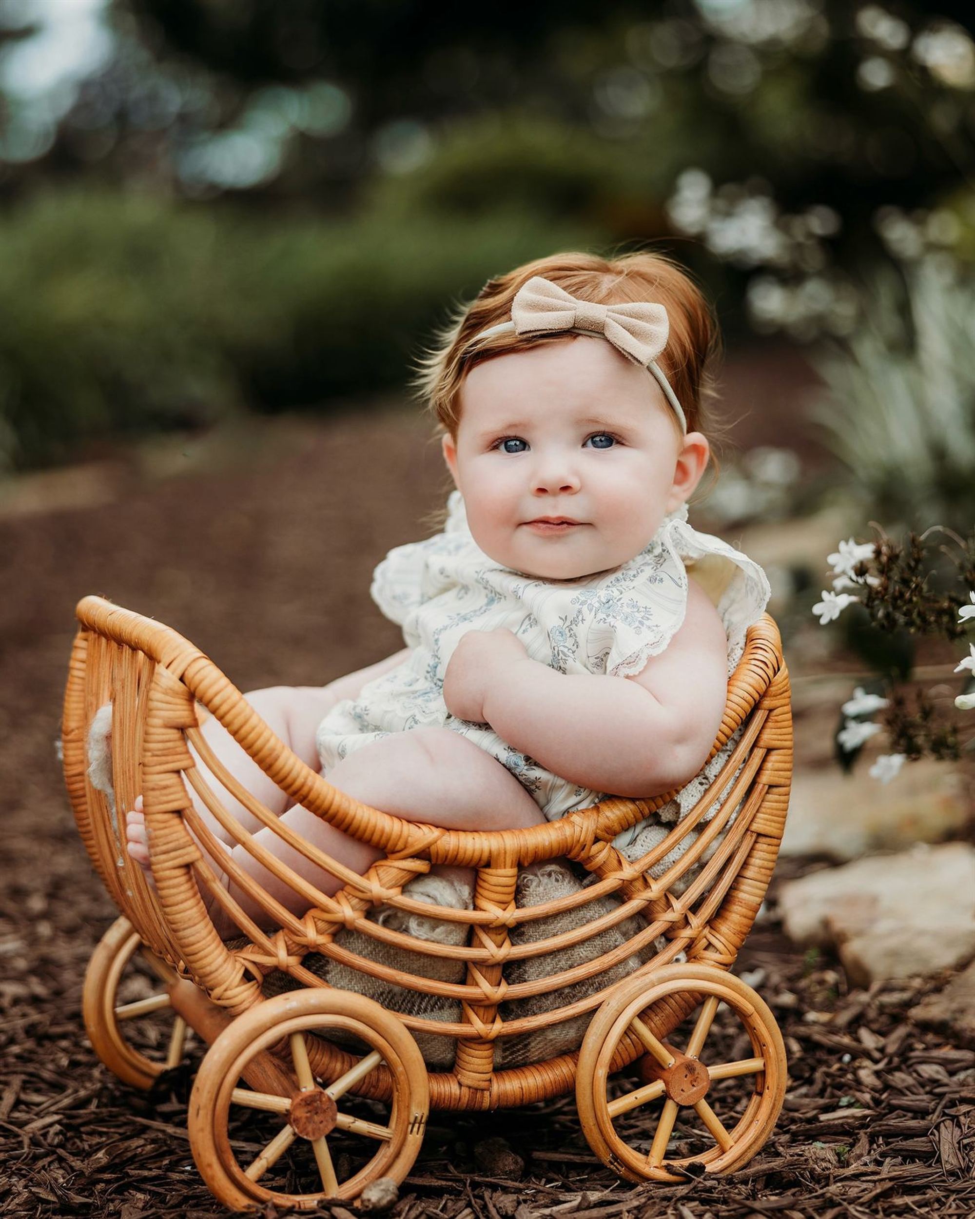 A baby girl in a bow headband sitting in a rattan carriage