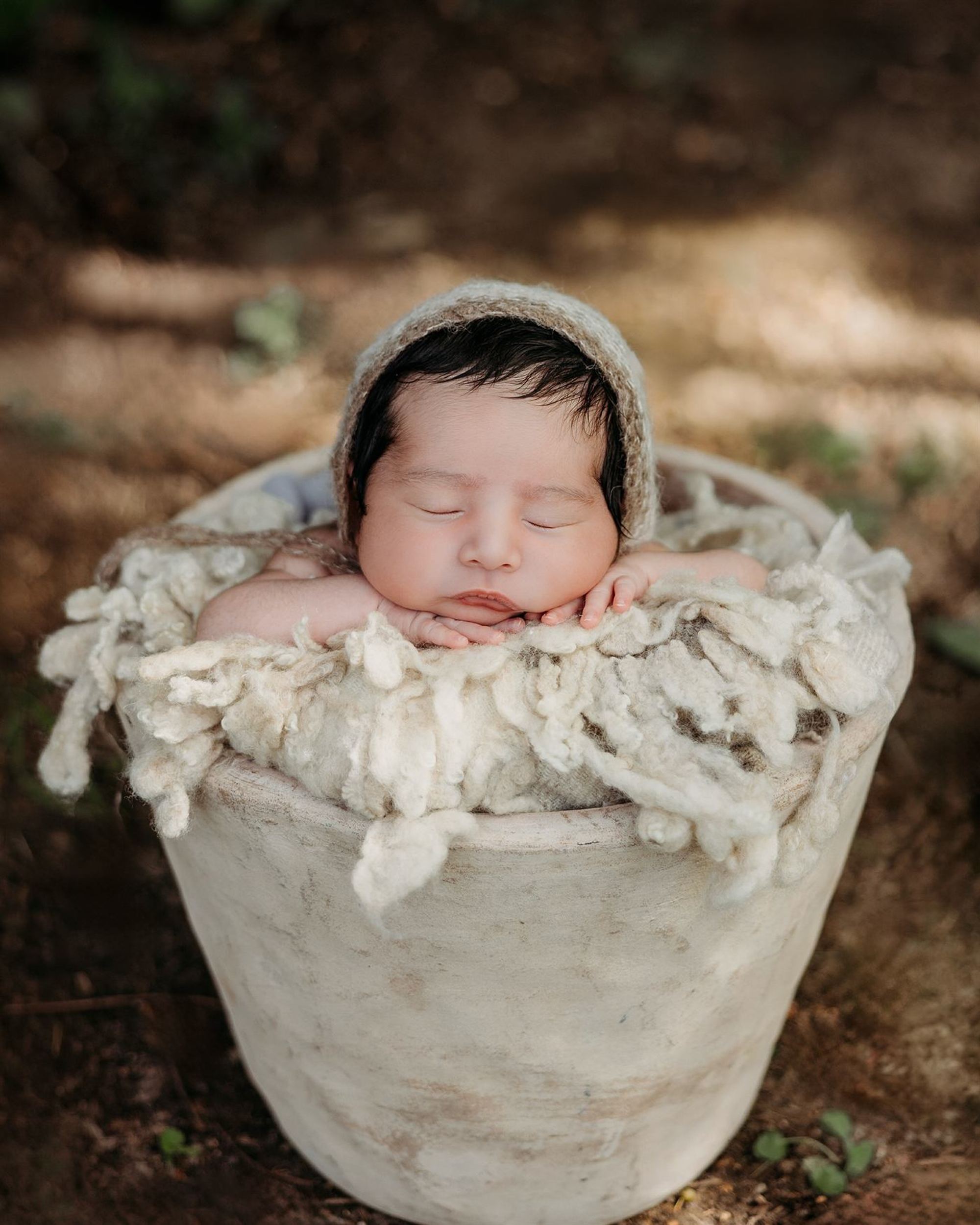 A newborn in a knit bonnet sleeping peacefully in a stone bowl
