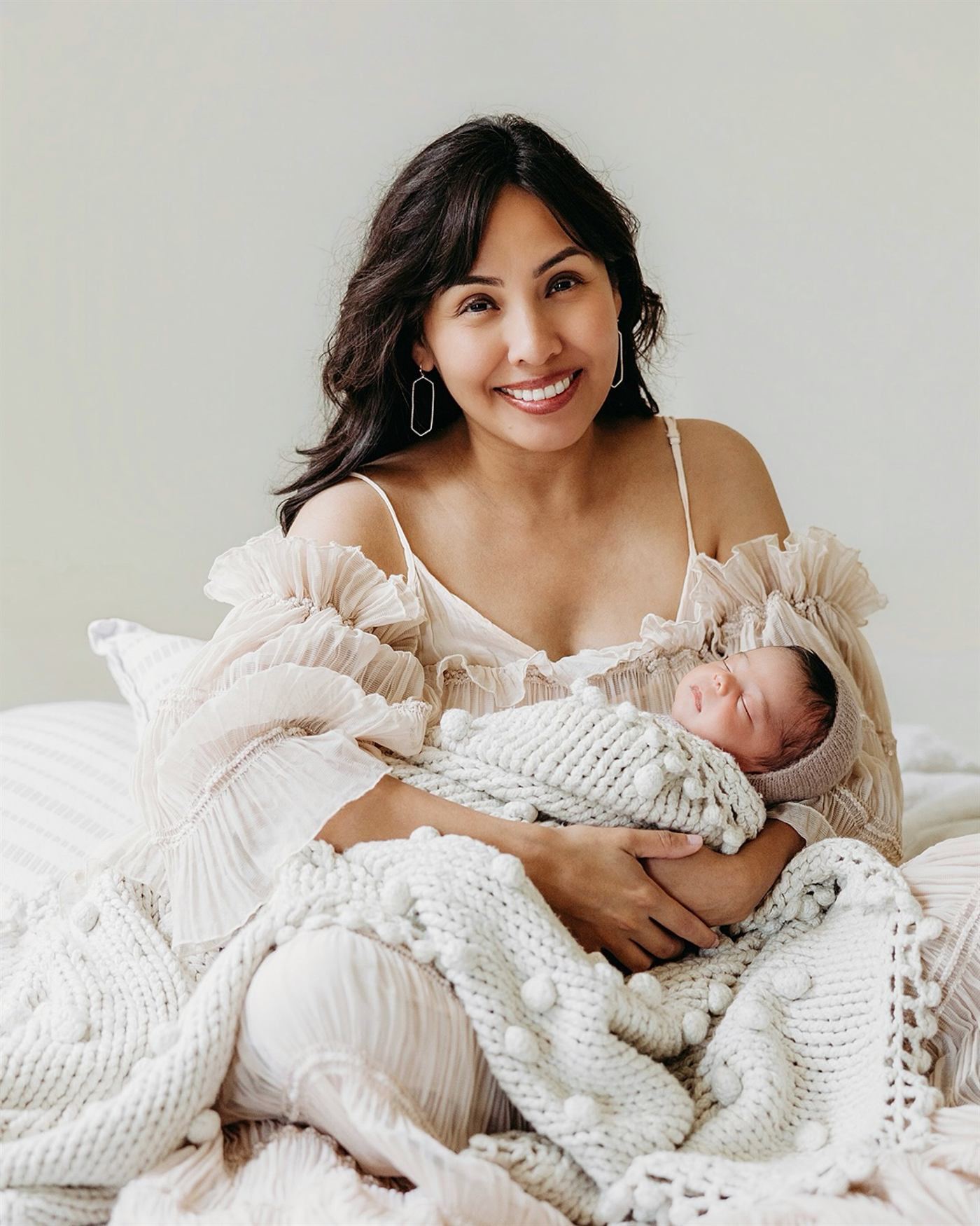 A smiling mother wrapped in lace, holding her sleeping newborn