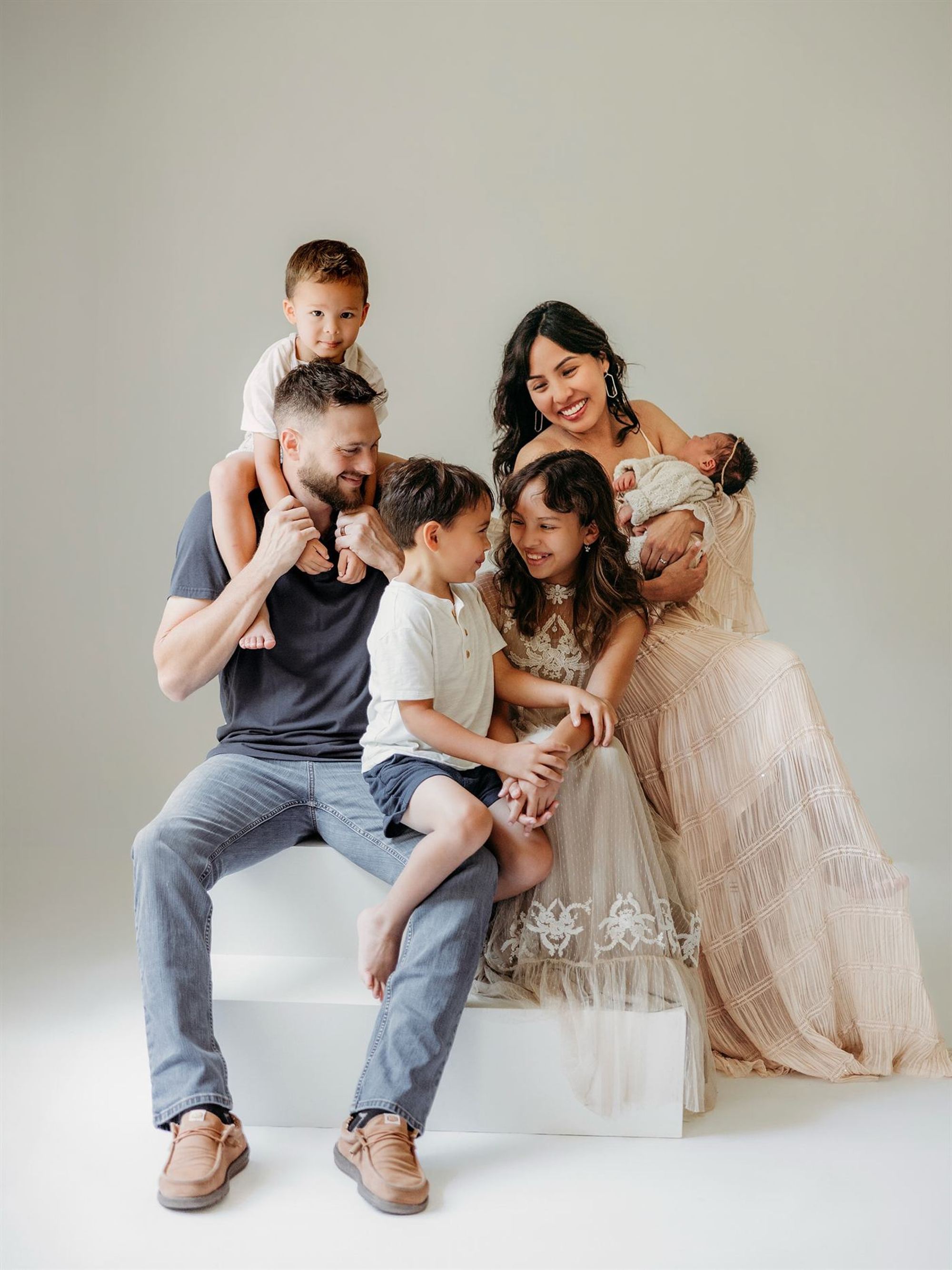 A family of six laughing together on white studio blocks