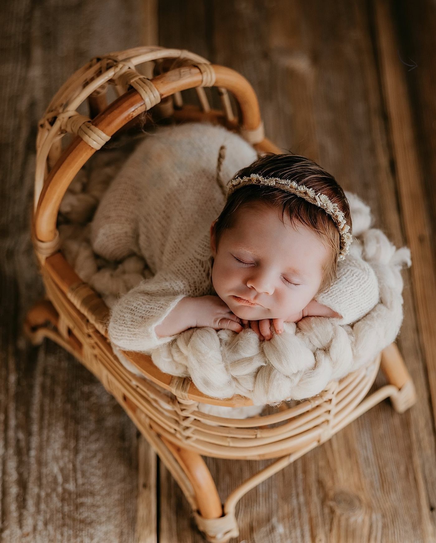 A newborn asleep on a cream knit in a small rattan chair