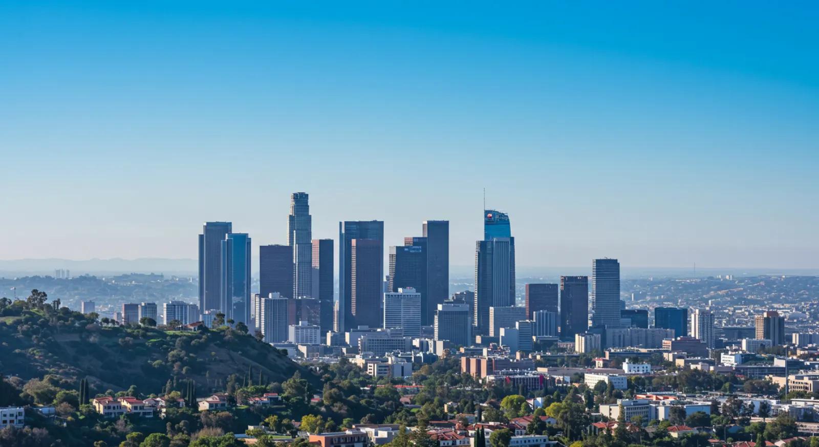 Downtown Los Angeles skyline seen from green hills under a clear blue sky