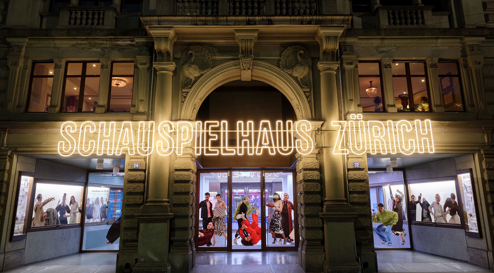 The Schauspielhaus Zürich theatre building at night, illuminated by a large neon sign and dynamic displays in its windows.