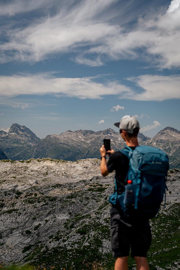 Der Fotograf Niklas Röhrl steht vor einer Bergkulisse und macht nimmt ein Bild auf.