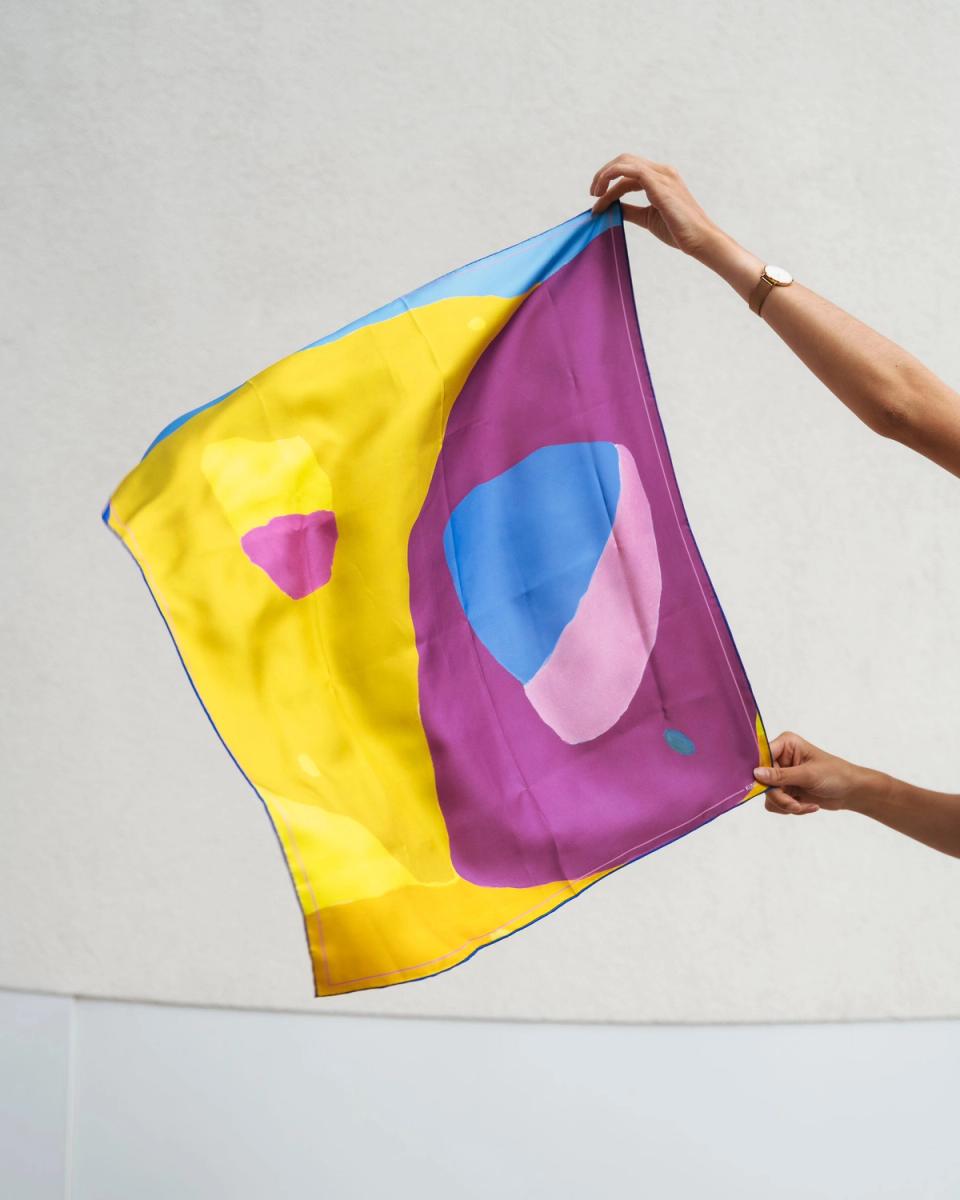 The Johs Rian scarf held up outdoors, showing the full yellow and purple abstract field