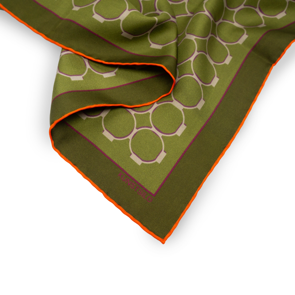 Corner detail of the Signature scarf in olive green — the ring motif and a contrasting orange rolled edge