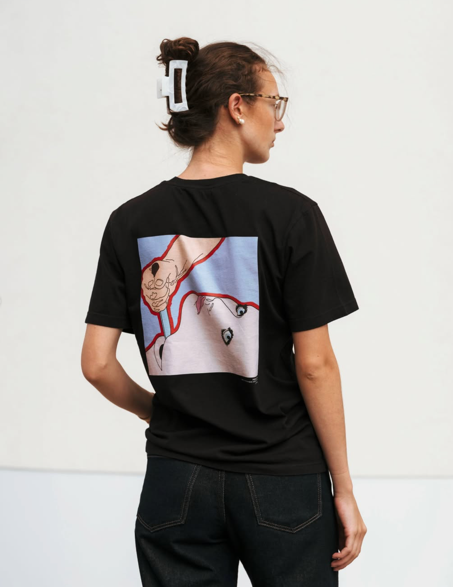 Back view of a model wearing a black Kunstsilo T-shirt — an expressive figurative print in blue and red from the Tangen Collection on the back panel