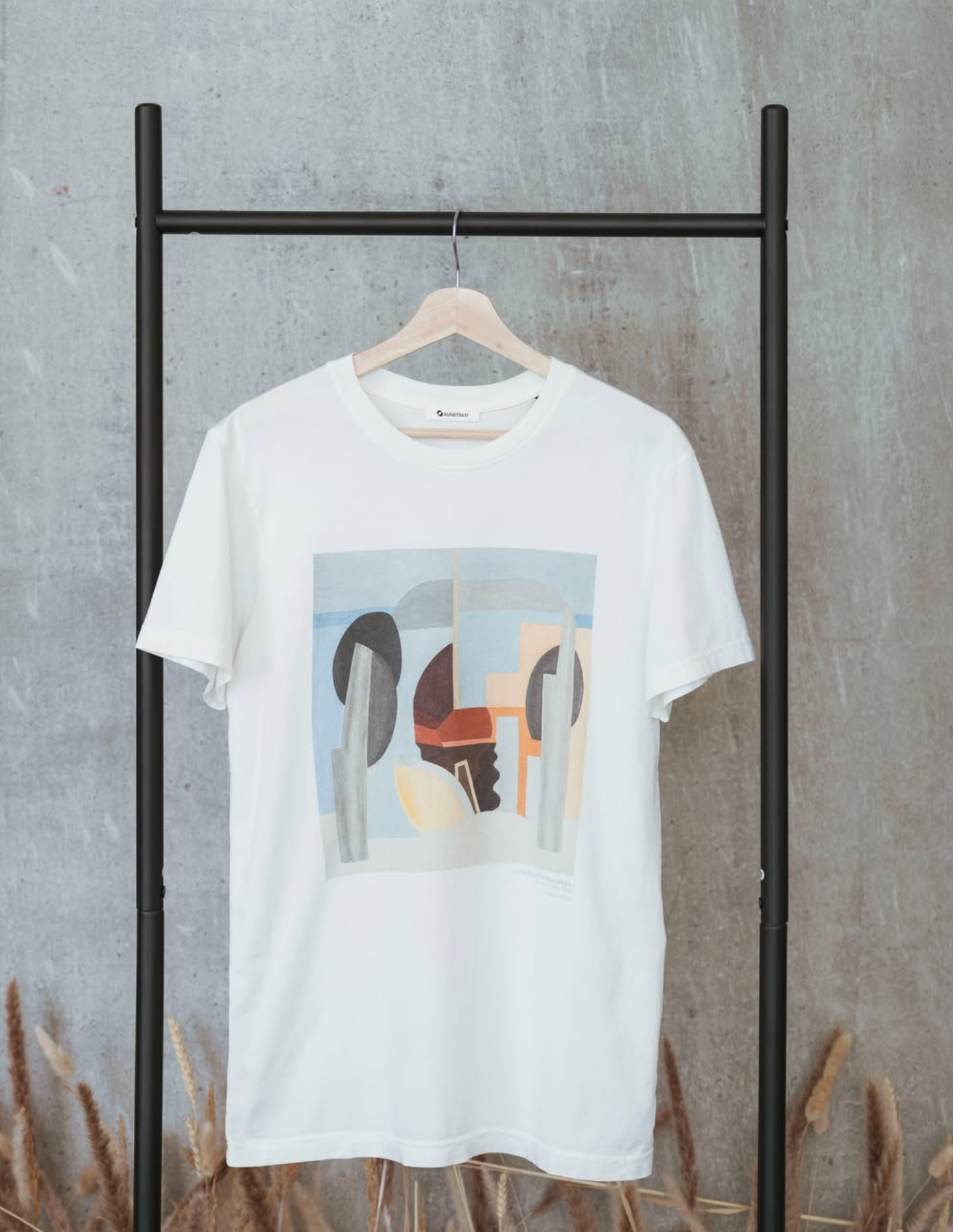 A white Kunstsilo T-shirt on a hanger — an abstract composition in muted blue, grey and rust tones from the Tangen Collection