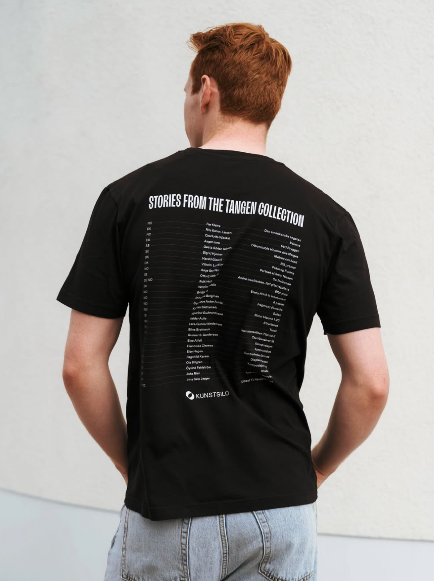 Back view of a man in a black Kunstsilo T-shirt — “Stories from the Tangen Collection” printed in white across the back, with a full artist listing and the Kunstsilo mark