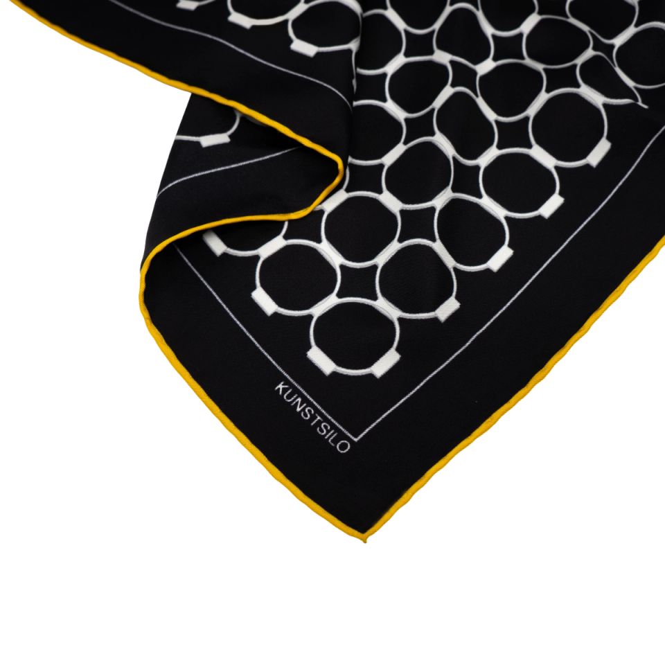Corner detail of the Signature scarf in black — white silo-ring pattern and yellow hand-rolled edge, "KUNSTSILO" label