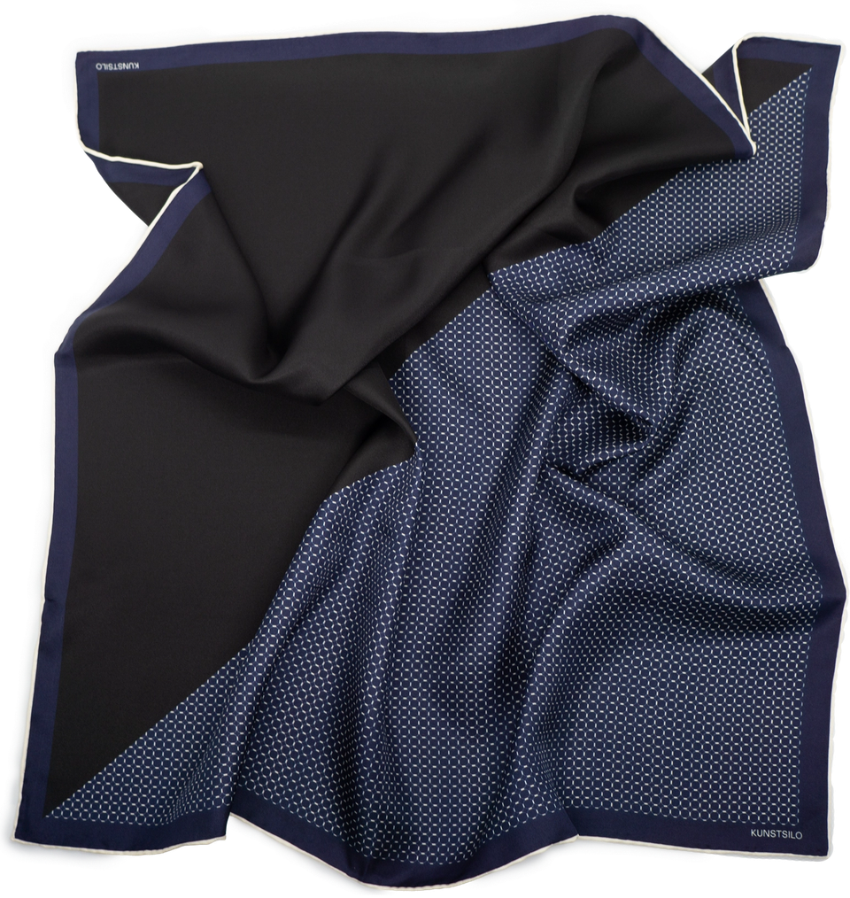 The Kunstsilo Signature Bandana in navy — two-sided silk, one face solid, one a fine dot repeat, with a cream rolled edge