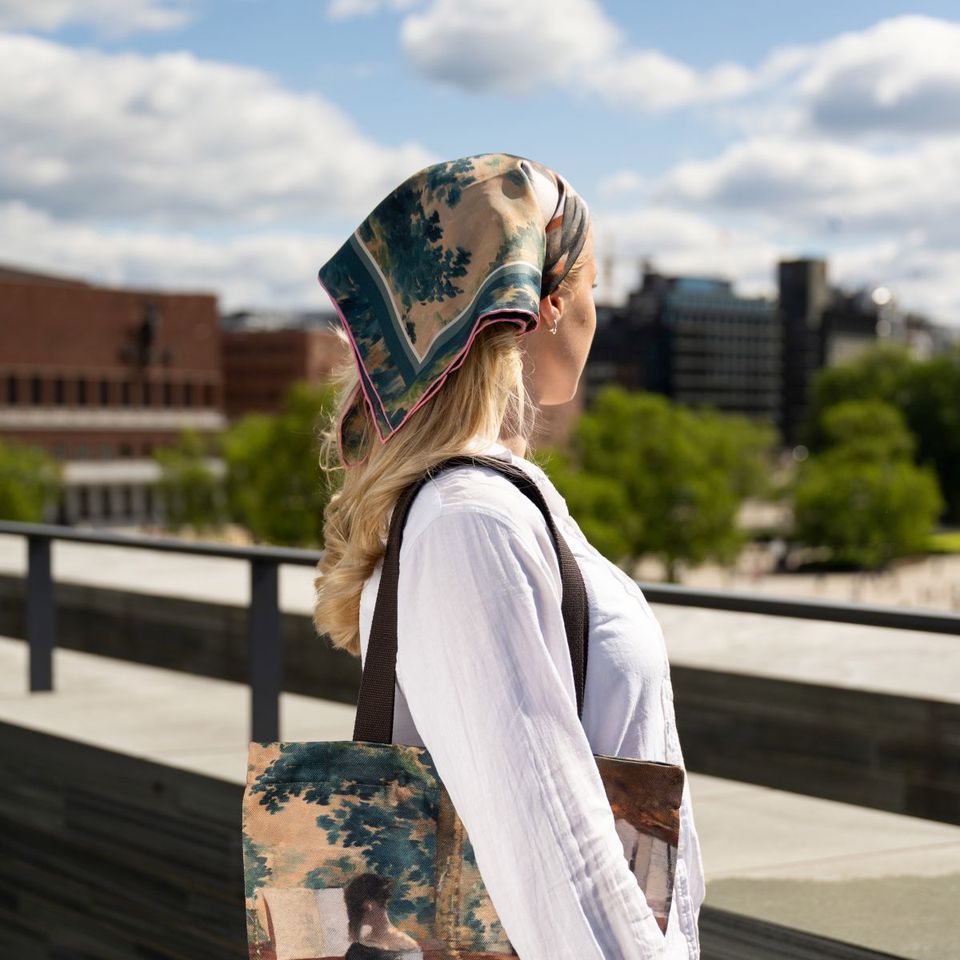 The Musikkinteriør scarf worn as a headscarf, with a matching tote, against the Oslo skyline