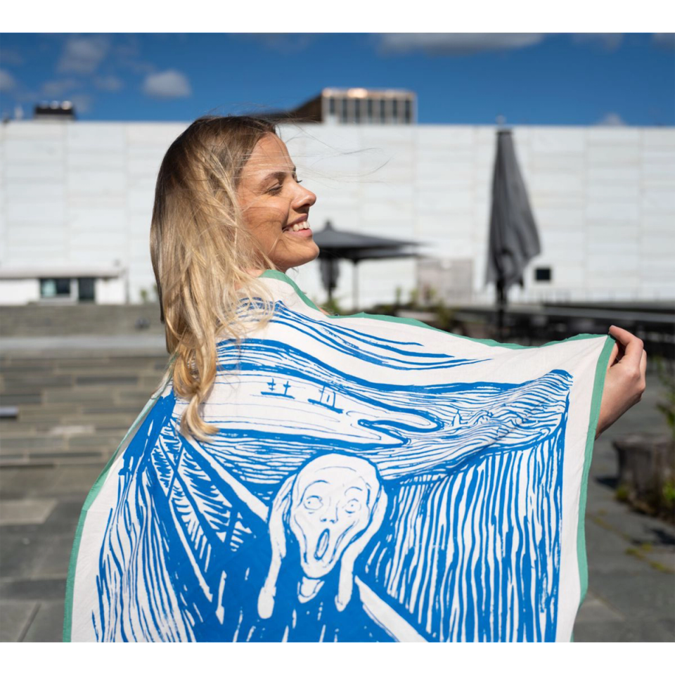 The Skrik scarf held wide by the Nasjonalmuseet — Munch’s image in blue on cream cotton, with a green edge, against the Oslo waterfront