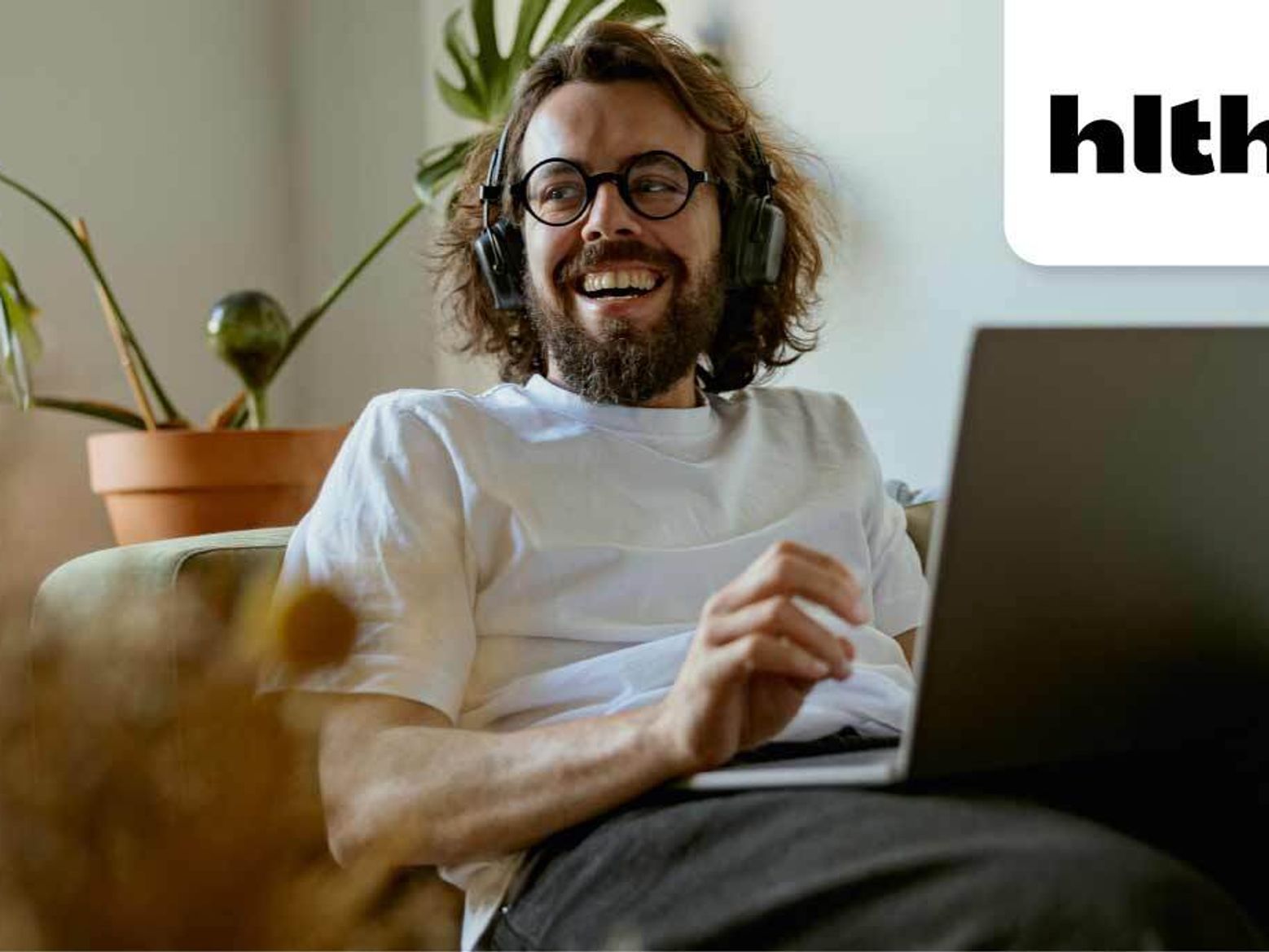 Adult male sitting on a couch with on a laptop. HTLH conference logo displayed next to him.