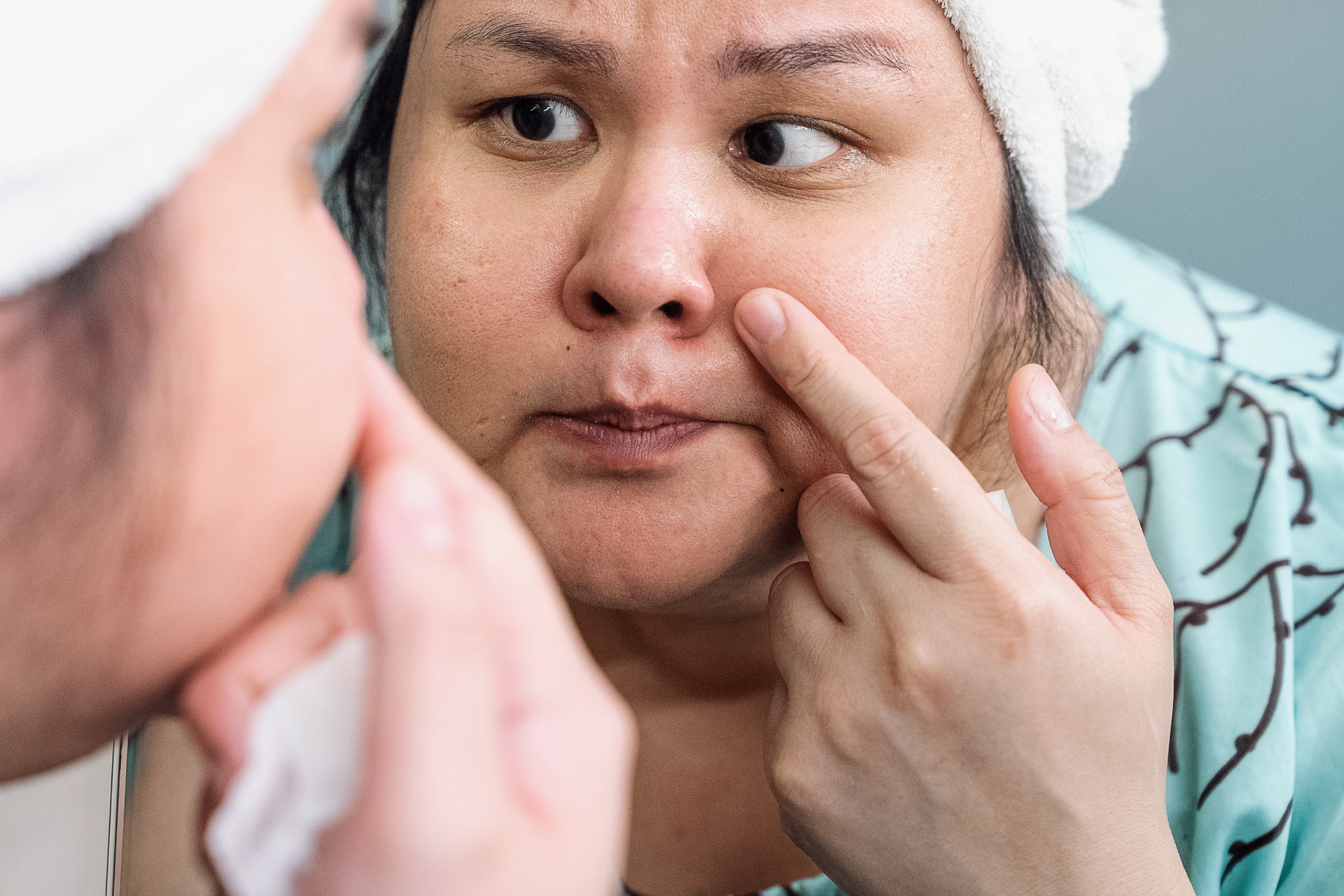 woman in bathrobe inspecting her skin in the mirrow 