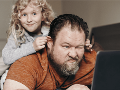 Adult male on laptop with child climbing on top of him