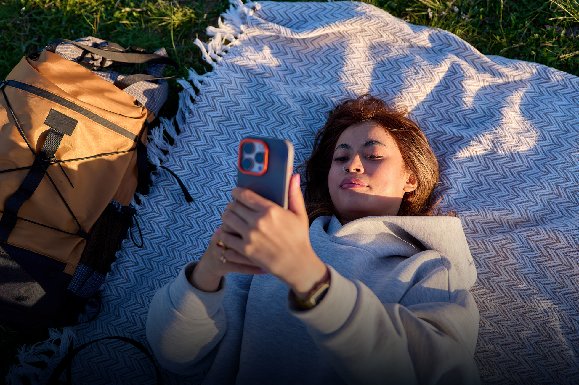 person lying on a picnic blanket outside looking at phone 