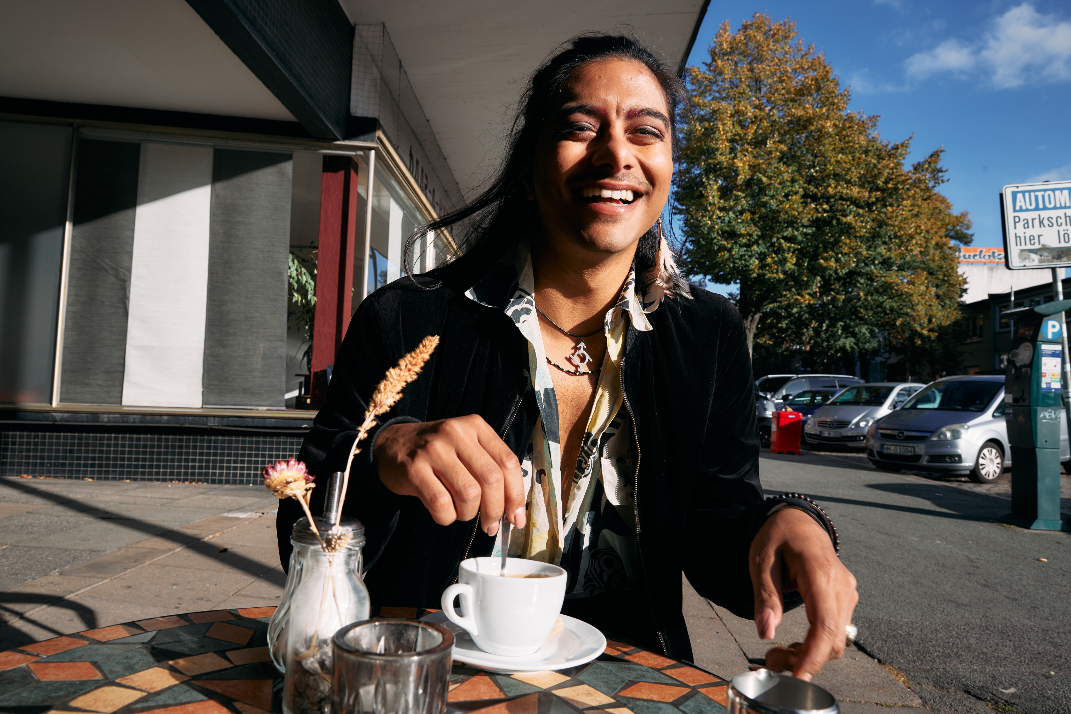 Person sitting outside on a nice day laughing while mixing coffee at a cafe