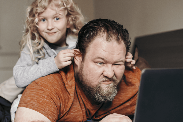 Adult male on laptop with child climbing on top of him