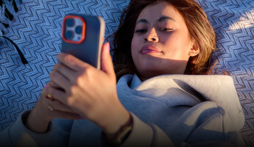 person lying on a picnic blanket outside looking at phone 