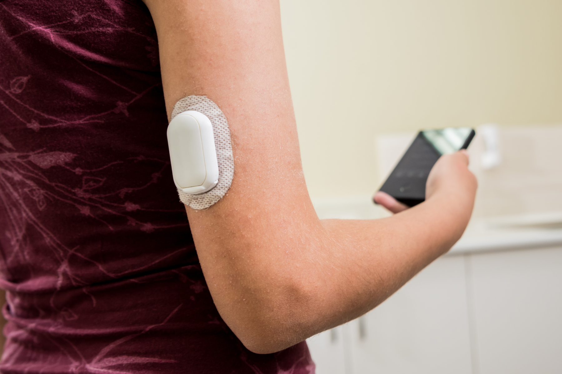 photograph of a blood glucose monitor on arm and phone in hand