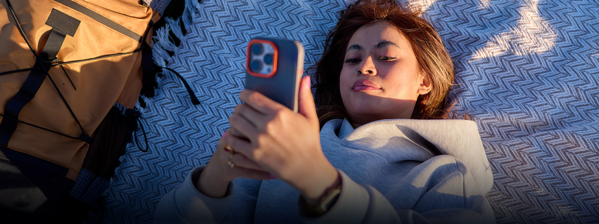 person lying on a picnic blanket outside looking at phone 