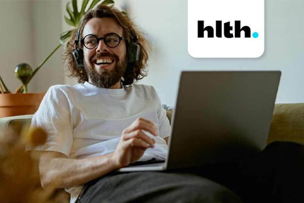 Adult male sitting on a couch with on a laptop. HTLH conference logo displayed next to him.