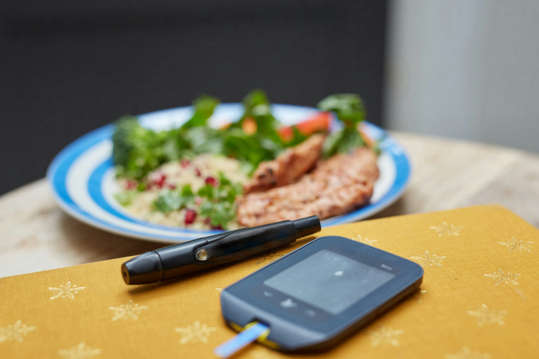 photo of a glucose monitor on a notebook. Healthy meal in the background