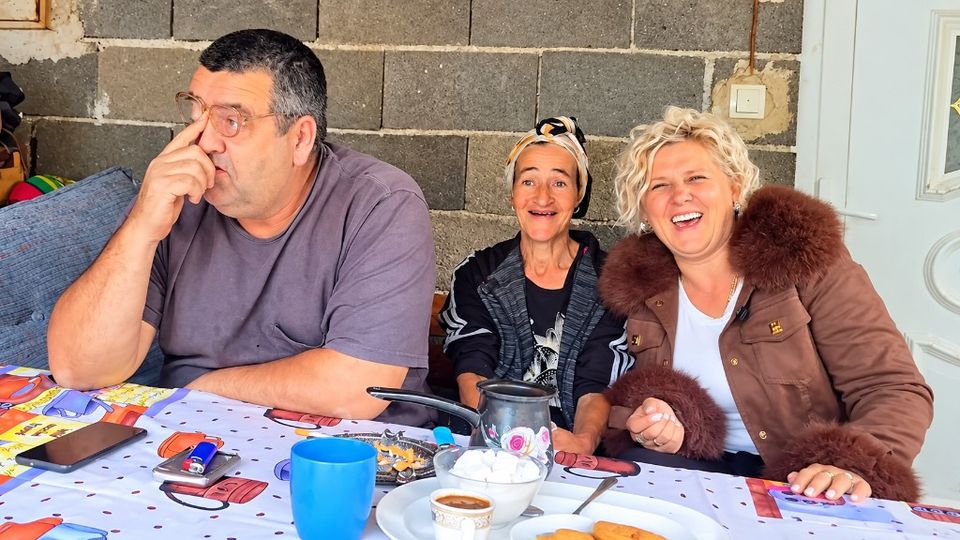 Muškarac s naočalama, starija žena s maramom i plavuša u braon jakni sjede za stolom uz kafu