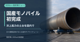 海辺の製造ヤードに置かれた巨大な鋼製モノパイルと洋上風車を背景に、「国産モノパイル初完成」と記した編集イメージ