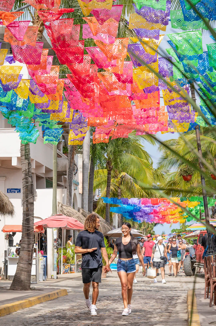Pareja caminando bajo colorido papel picado en la calle concurrida de Sayulita, durante un tour con Vallarta Adventures.