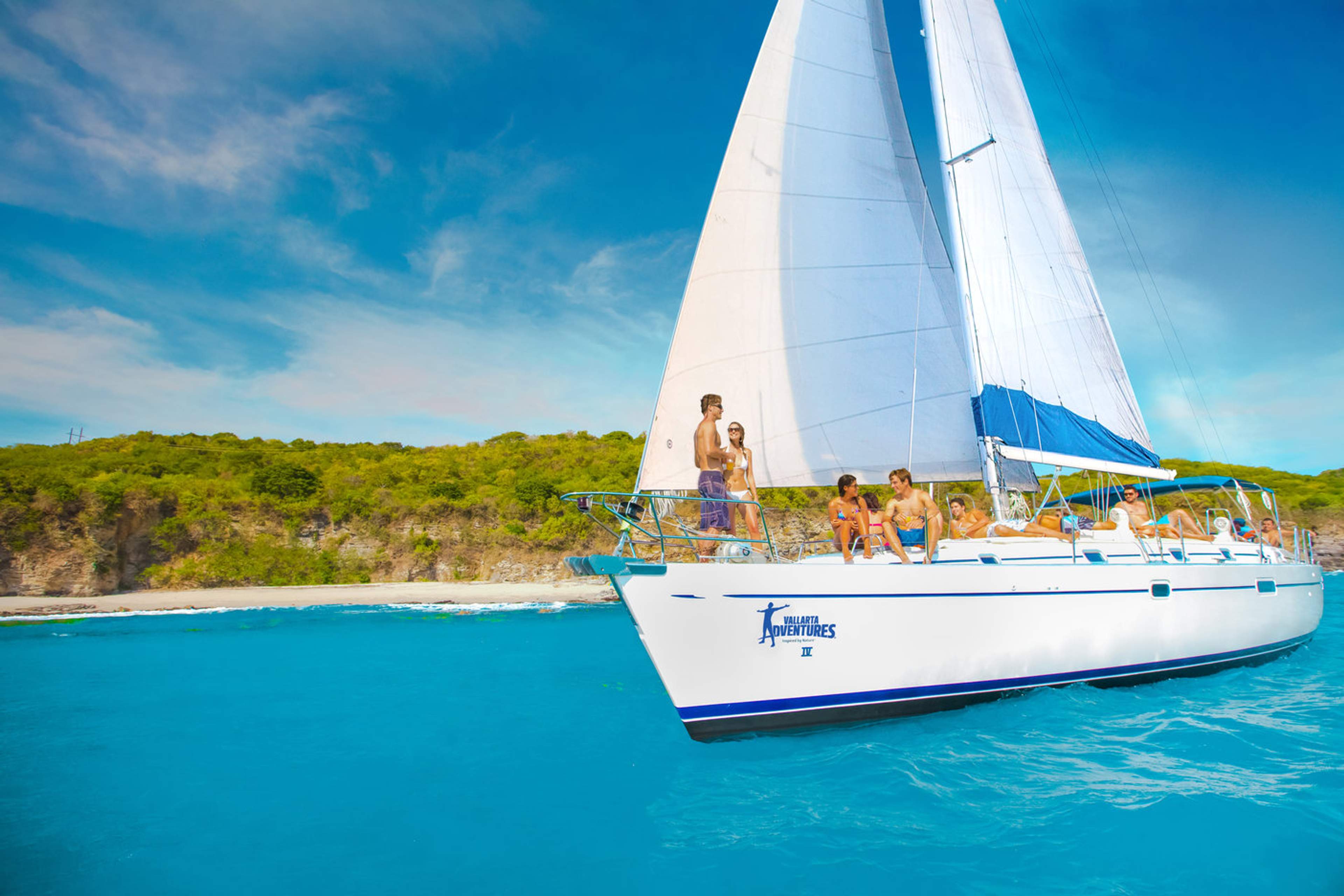 A group of people enjoy a sunny day sailing on a luxury boat near a scenic coastline.