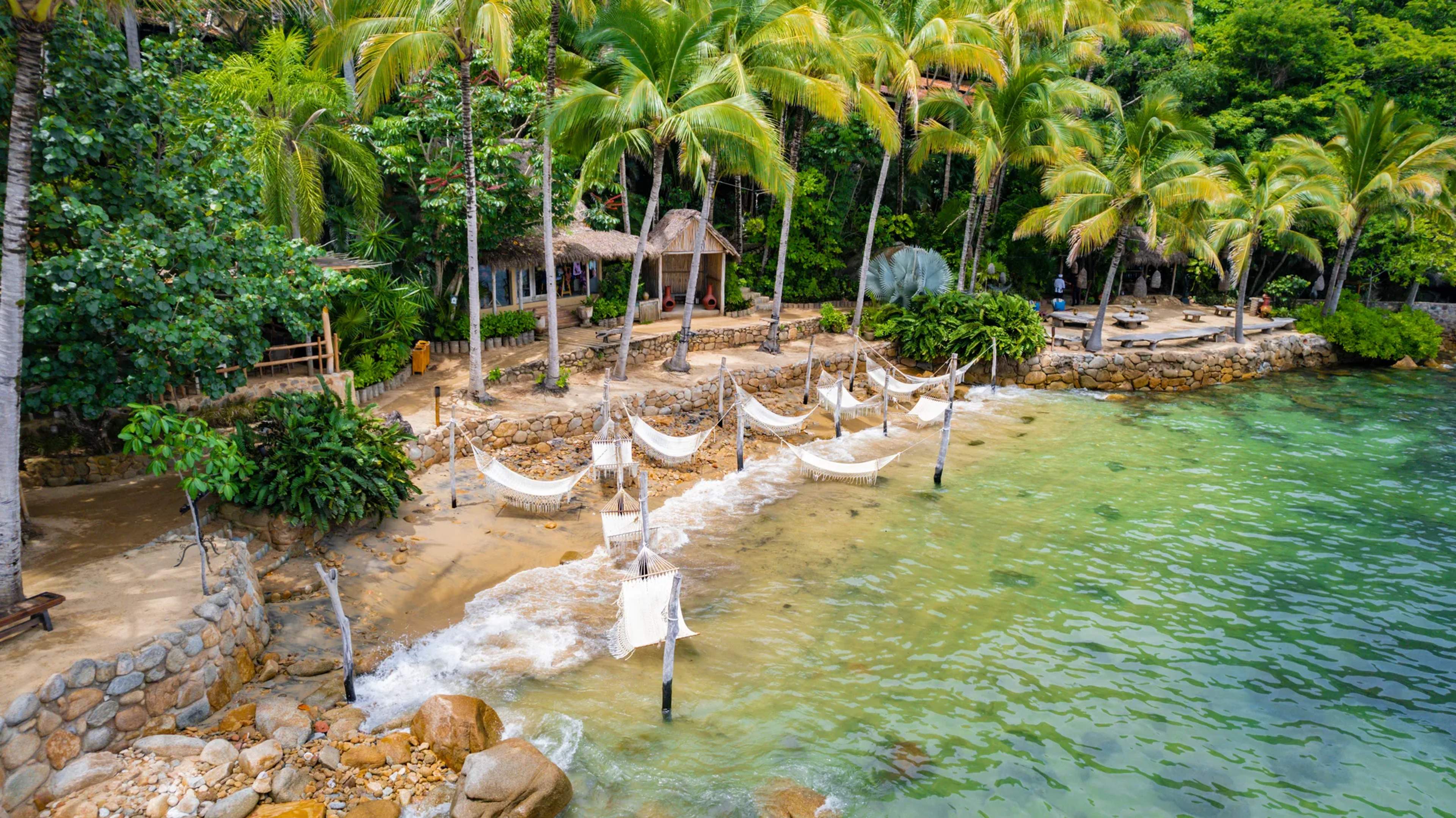 Hamacas blancas colgadas a orillas del mar en Las Caletas, enmarcadas por palmeras tropicales y aguas turquesas cristalinas.