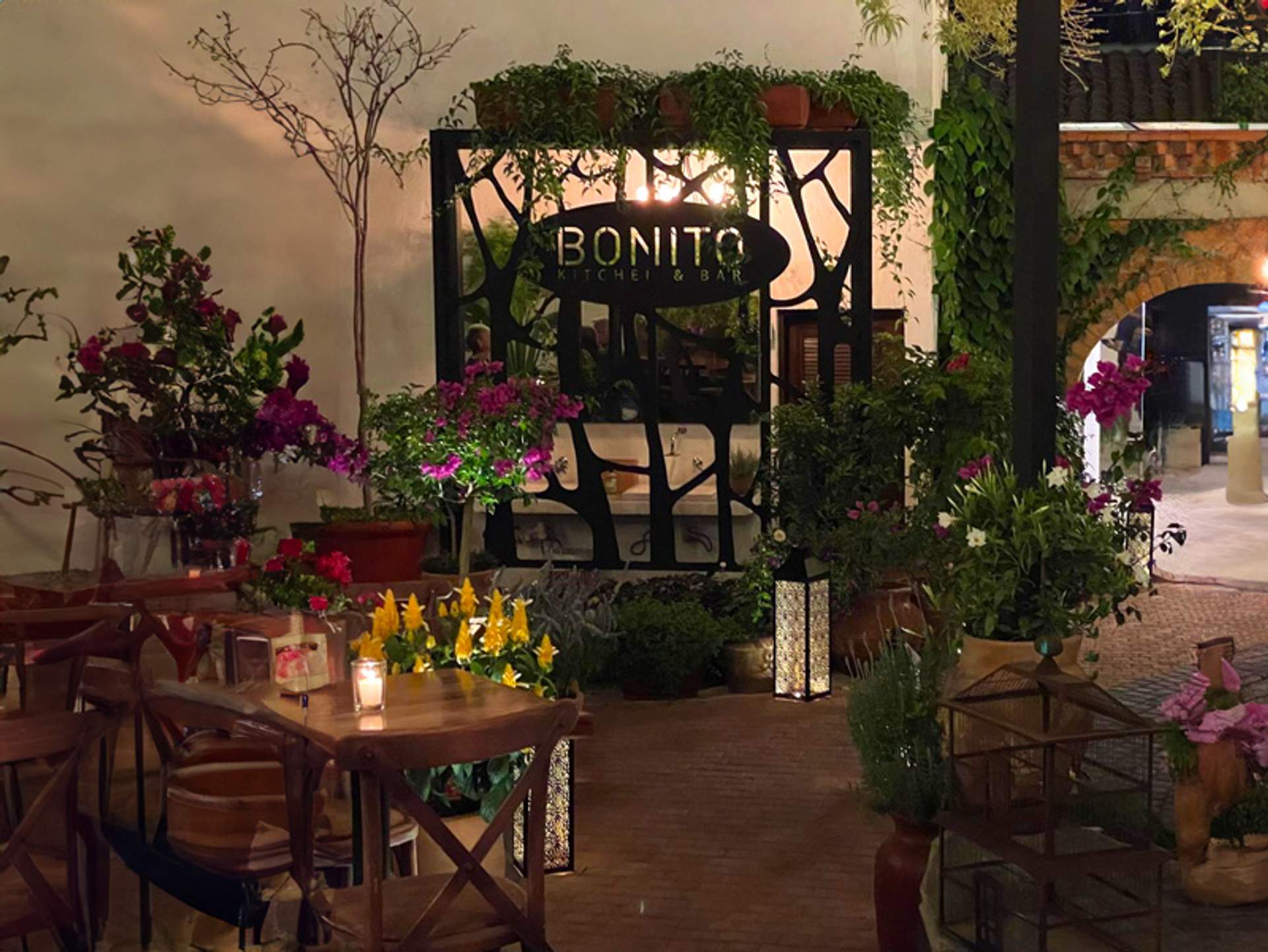 Outdoor seating at Bonito Kitchen & Bar, surrounded by lush greenery and vibrant flowers, creating a cozy ambiance.