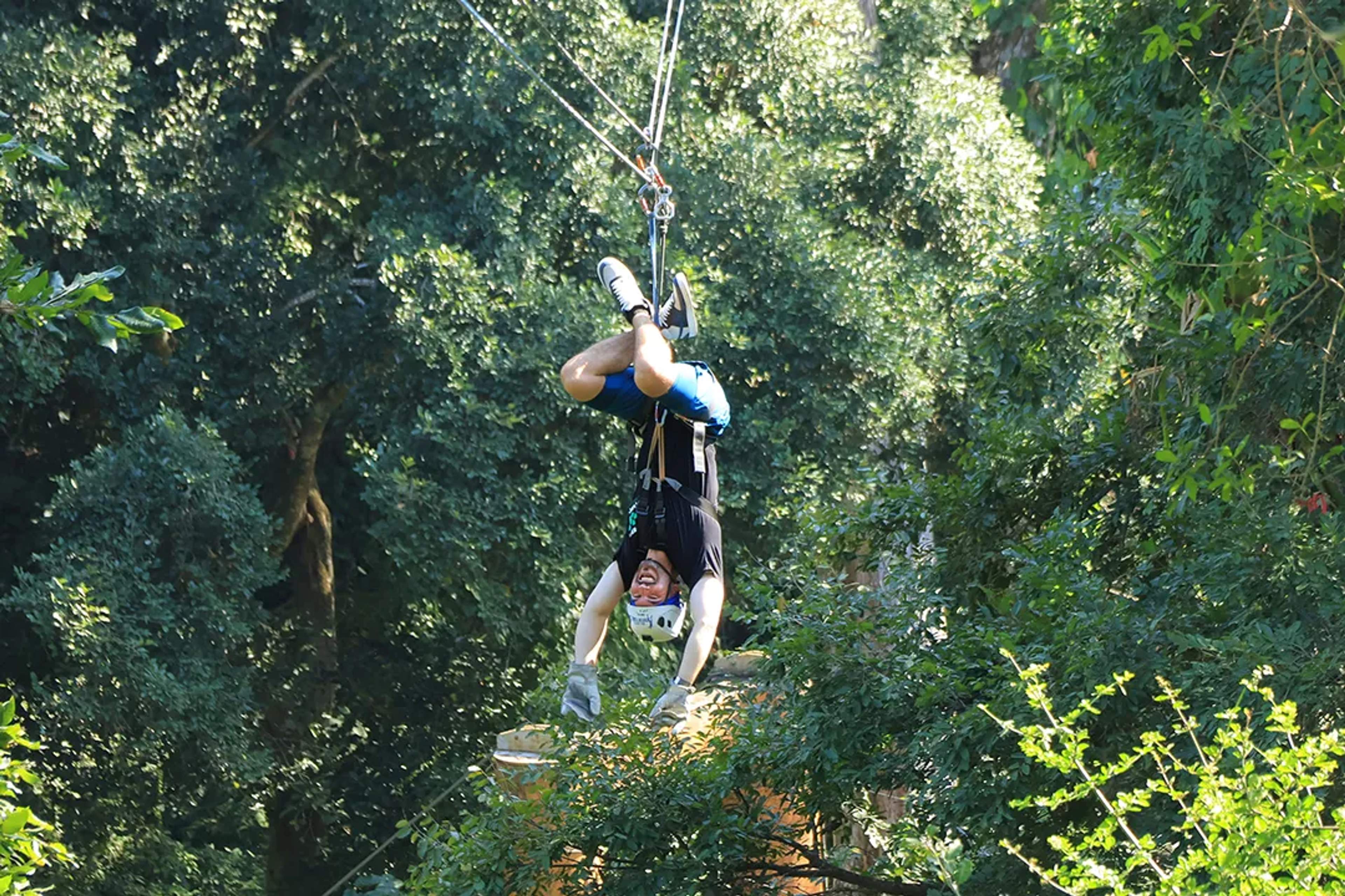 Hombre en tirolesa de cabeza atravesando la selva, sonriendo y disfrutando la adrenalina.