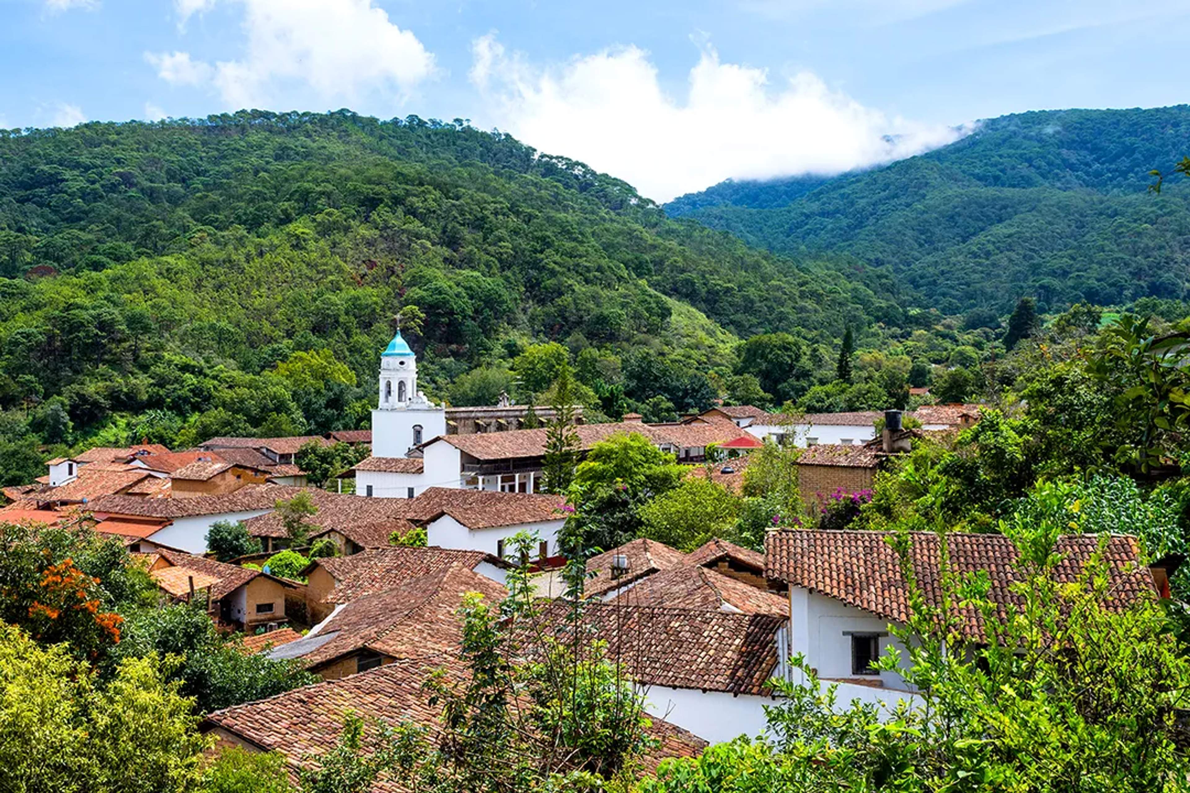 Colonial rooftops and church tower of San Sebastián del Oeste, surrounded by lush mountains.