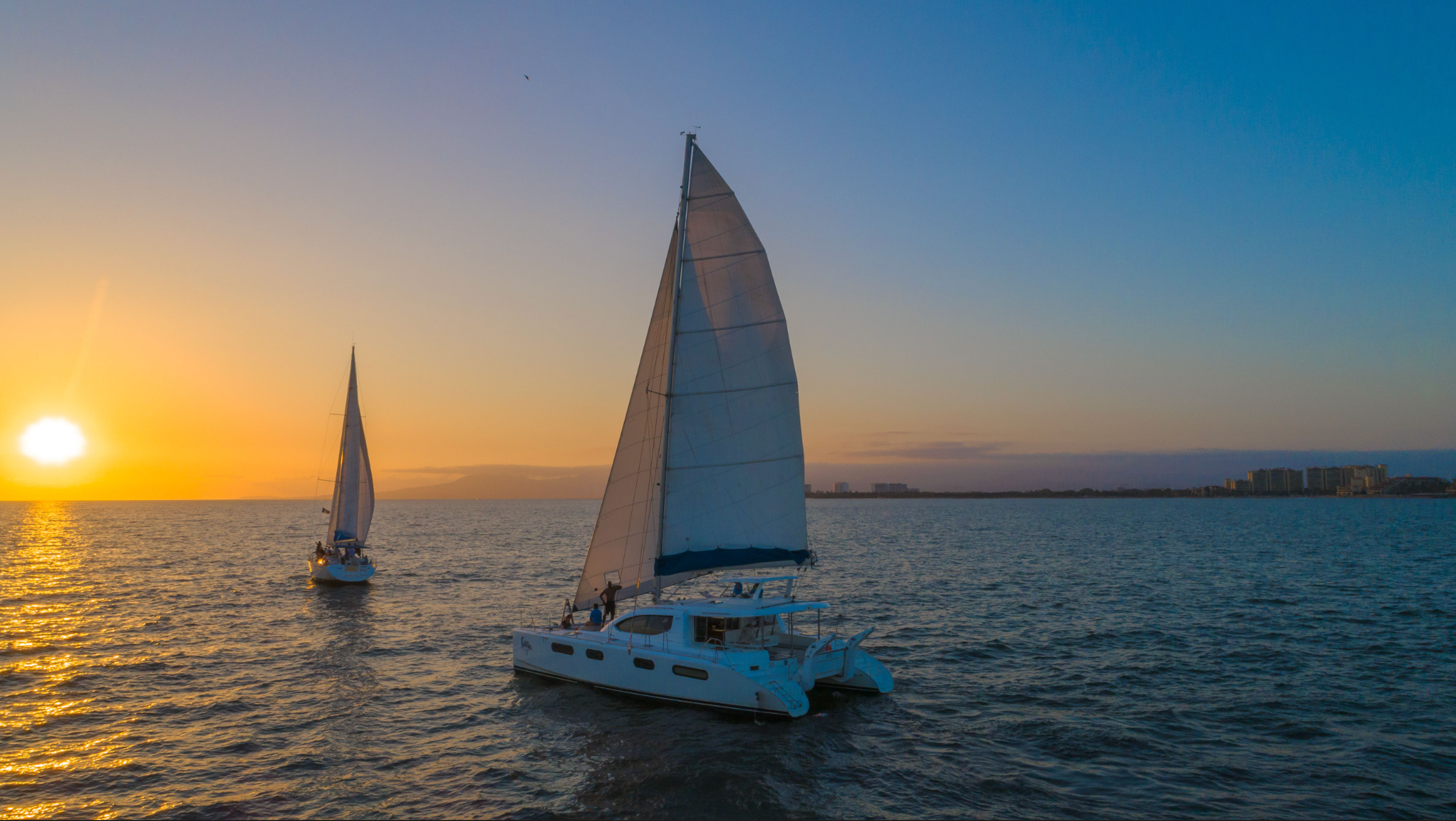 Two sailboats gliding on the ocean at sunset with Vallarta Adventures, showcasing a tranquil seascape.