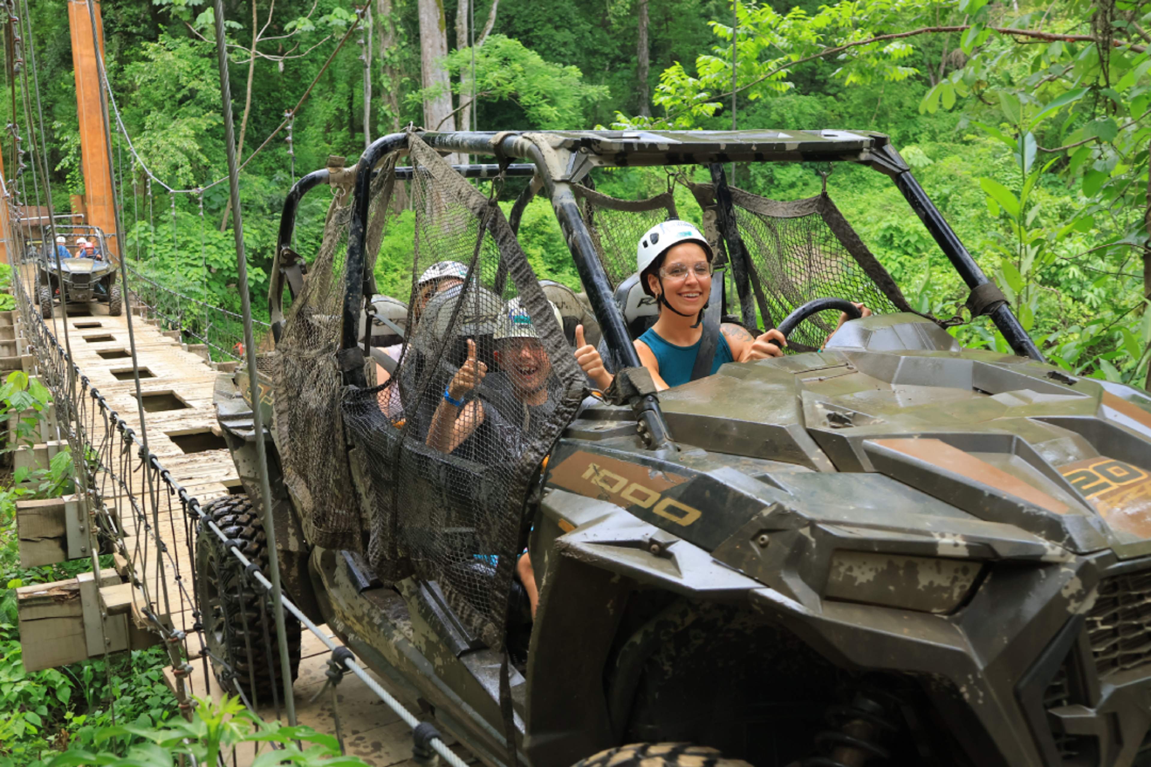 Aventureros cruzan un puente colgante en UTV, sonriendo en una travesía llena de adrenalina.
