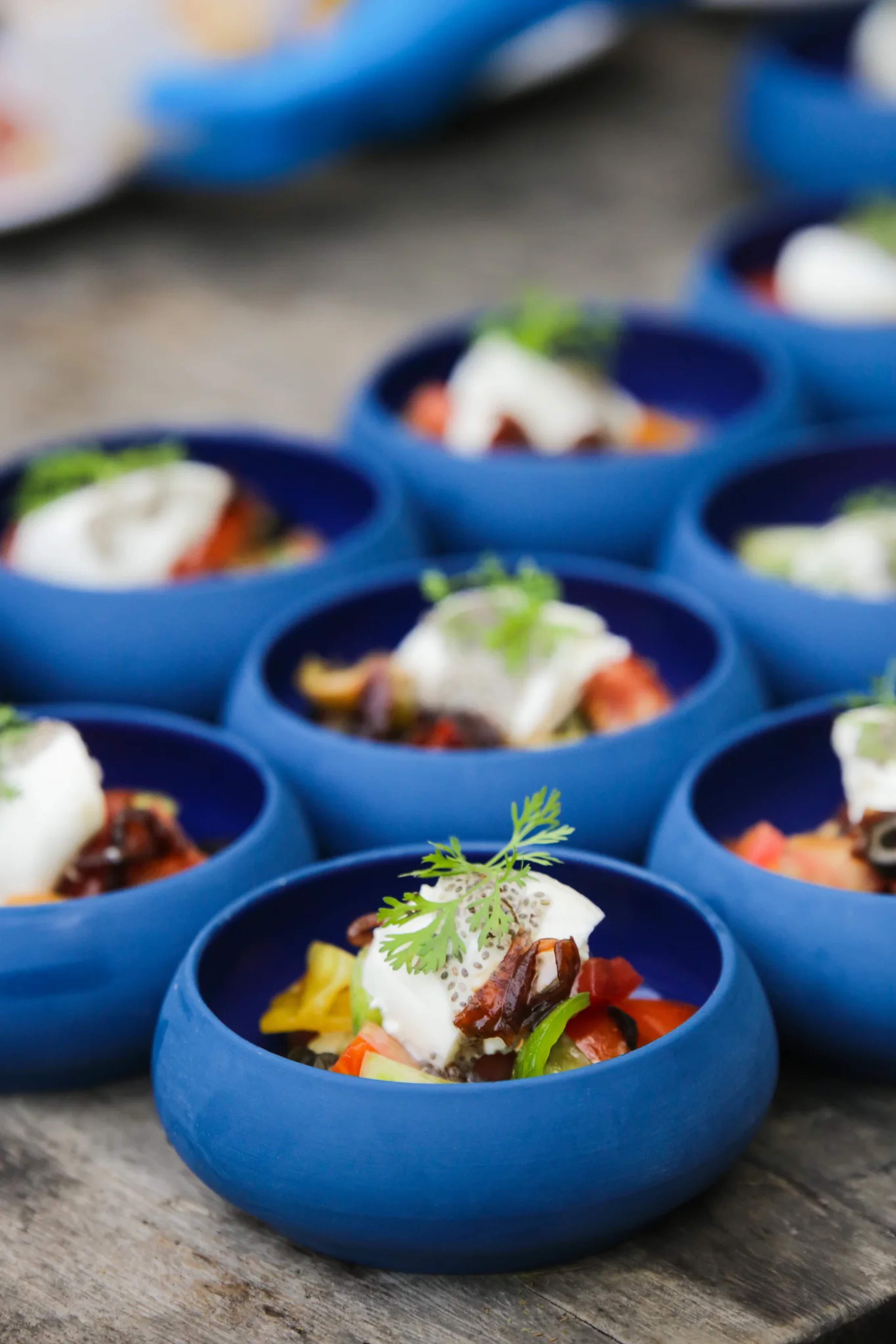 Gourmet appetizers in blue bowls with fresh ingredients and cilantro garnish, showcasing Pacific coastal flavors.
