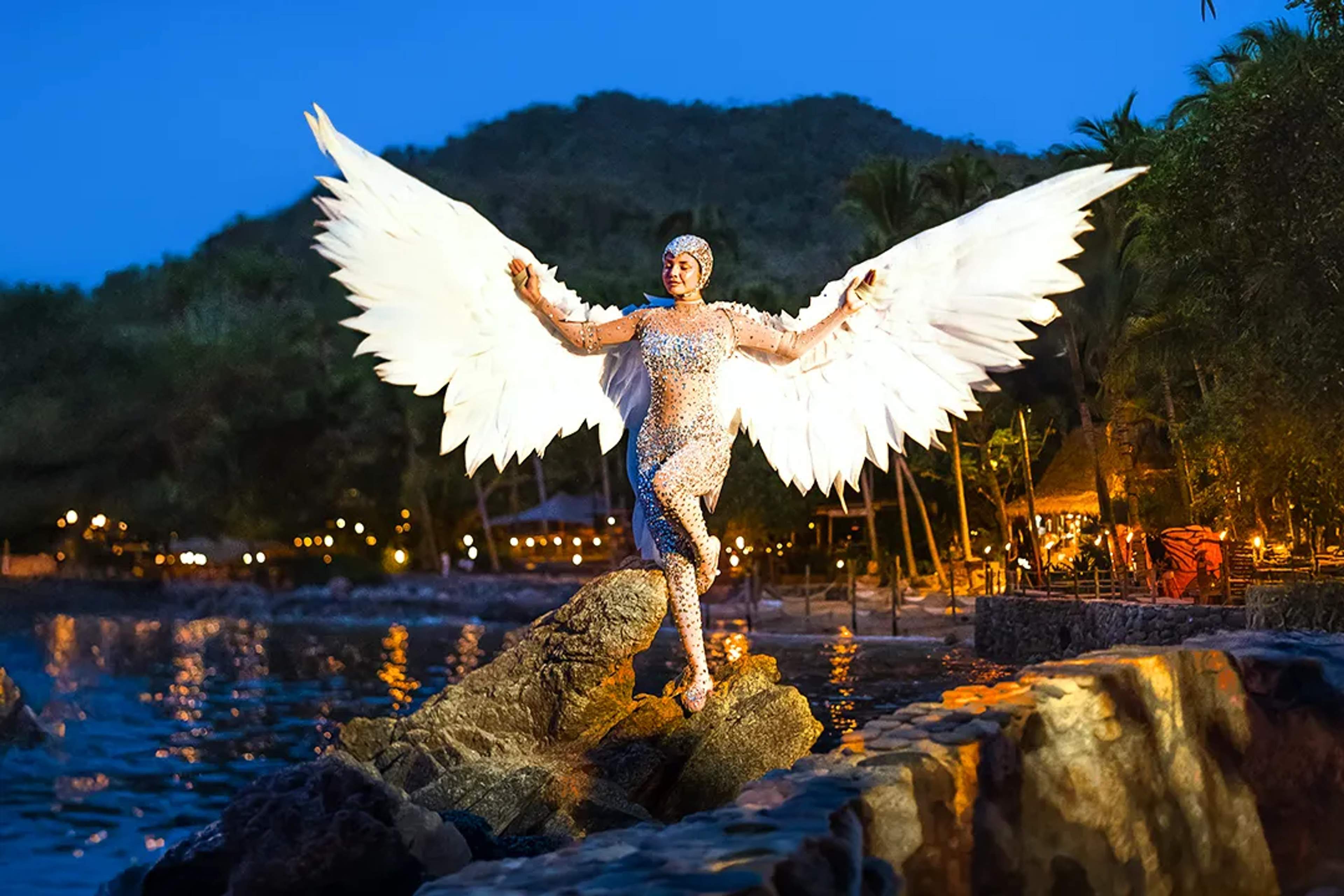 Rhythms of the Night performer at Las Caletas with angel wings, jungle stage and oceanfront setting