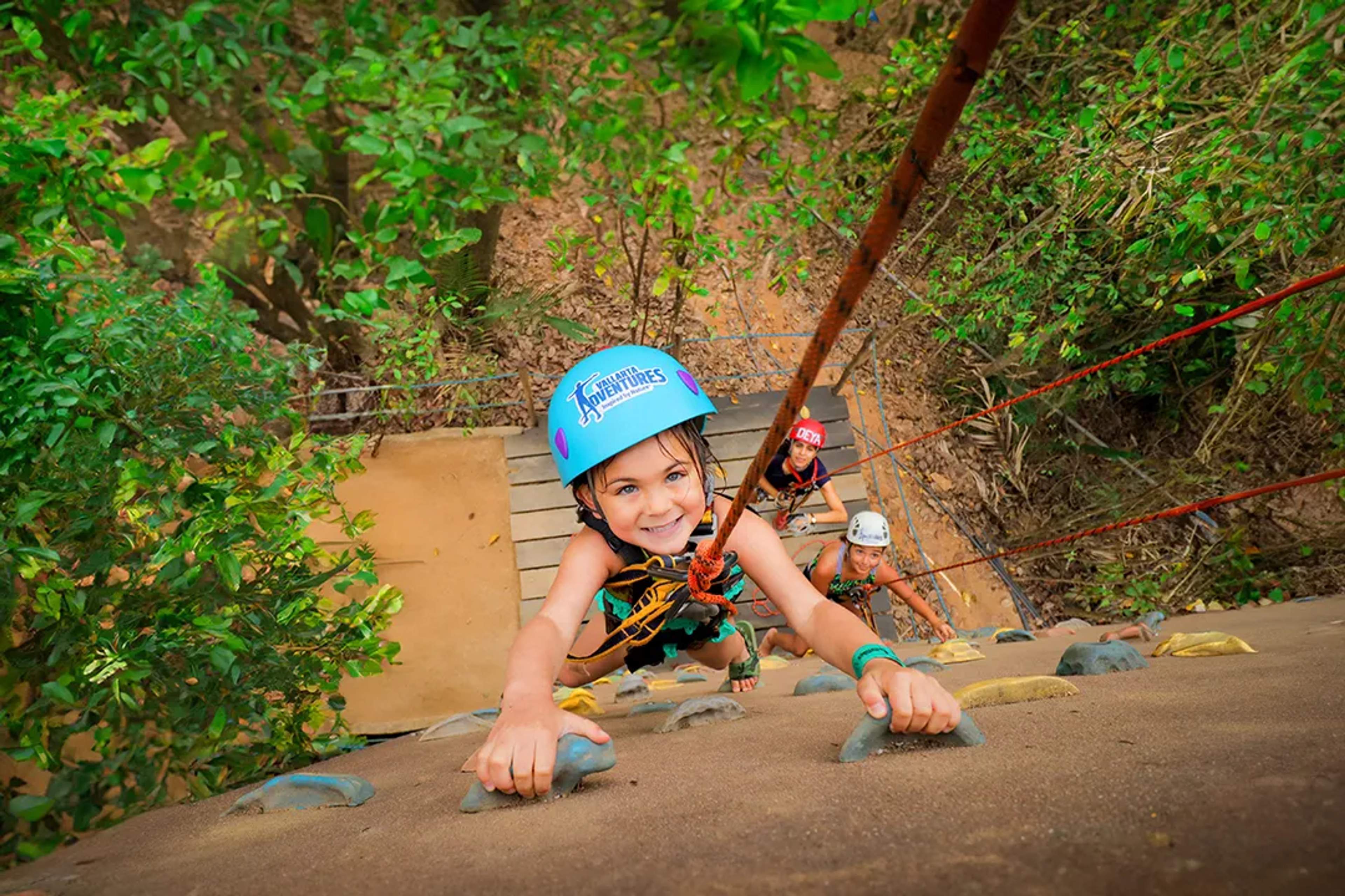 Niño escalando un muro en la selva en el Kids Adventure Park de Vallarta Adventures con equipo de seguridad