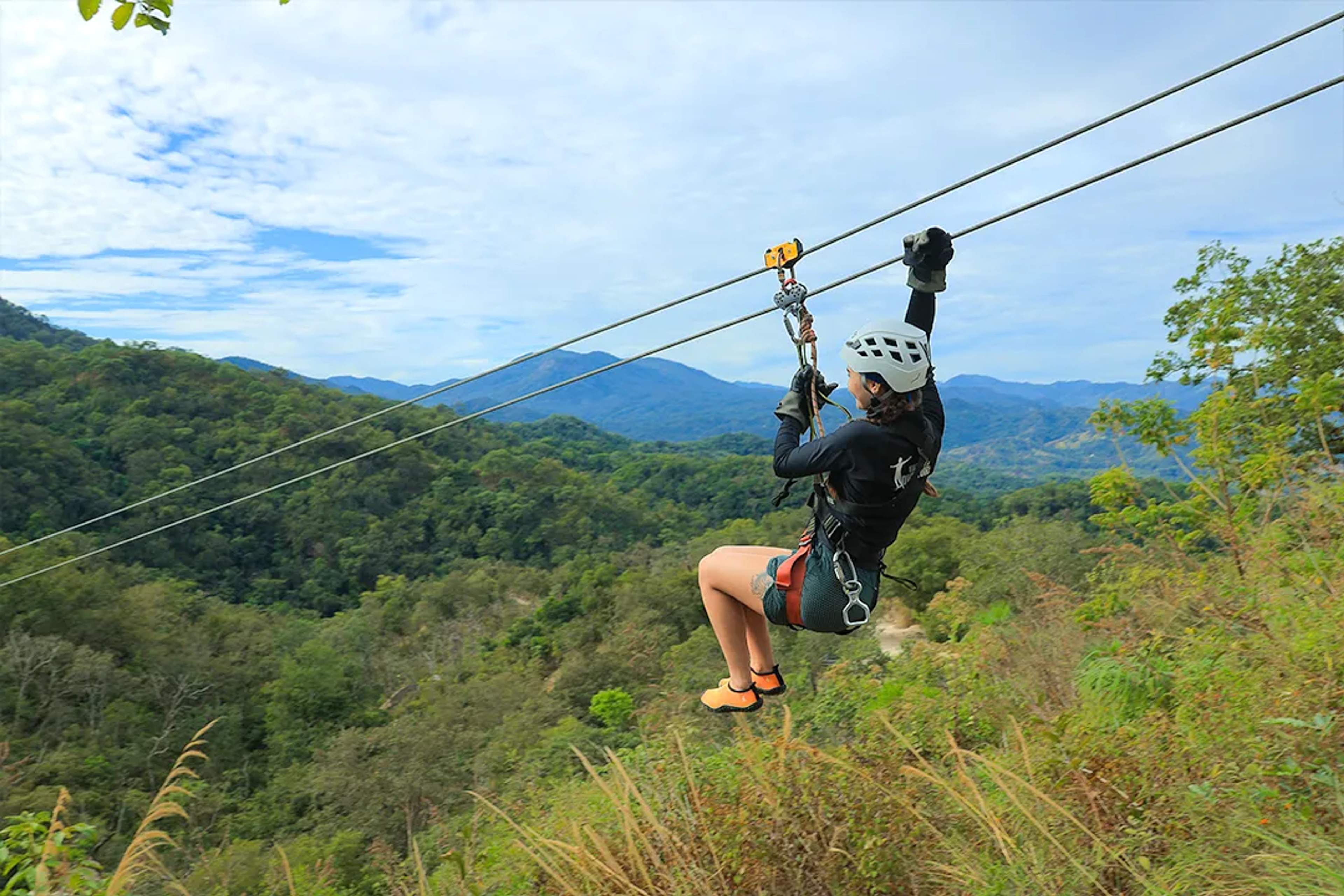 Woman zip-lining over lush jungle mountains, enjoying an adrenaline-filled adventure with panoramic nature views