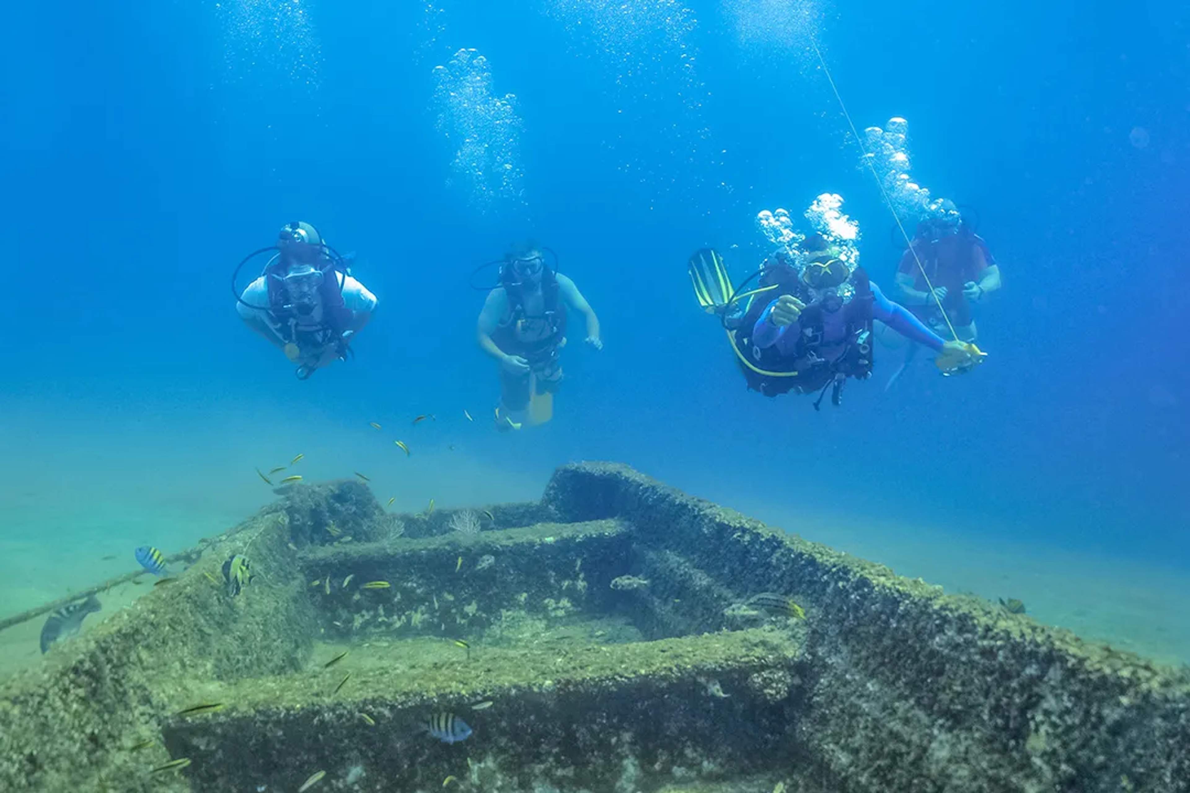 Group of scuba divers explore a shallow shipwreck surrounded by tropical fish the clear waters of Las Caletas, in Puerto Vallarta.