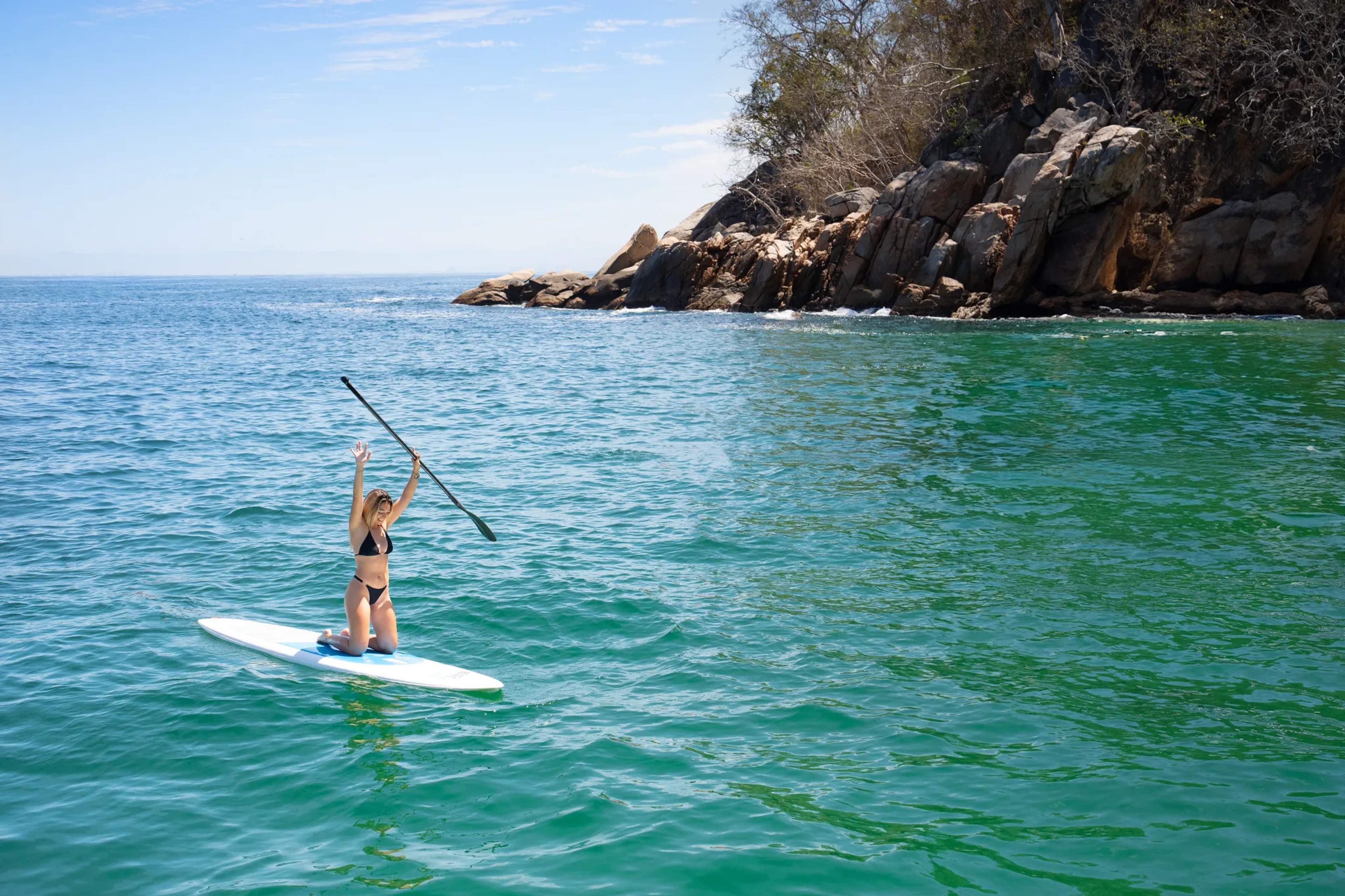 Un practicante de paddleboard rema en aguas turquesas de Majahuitas con acantilados rocosos y vegetación tropical al fondo.