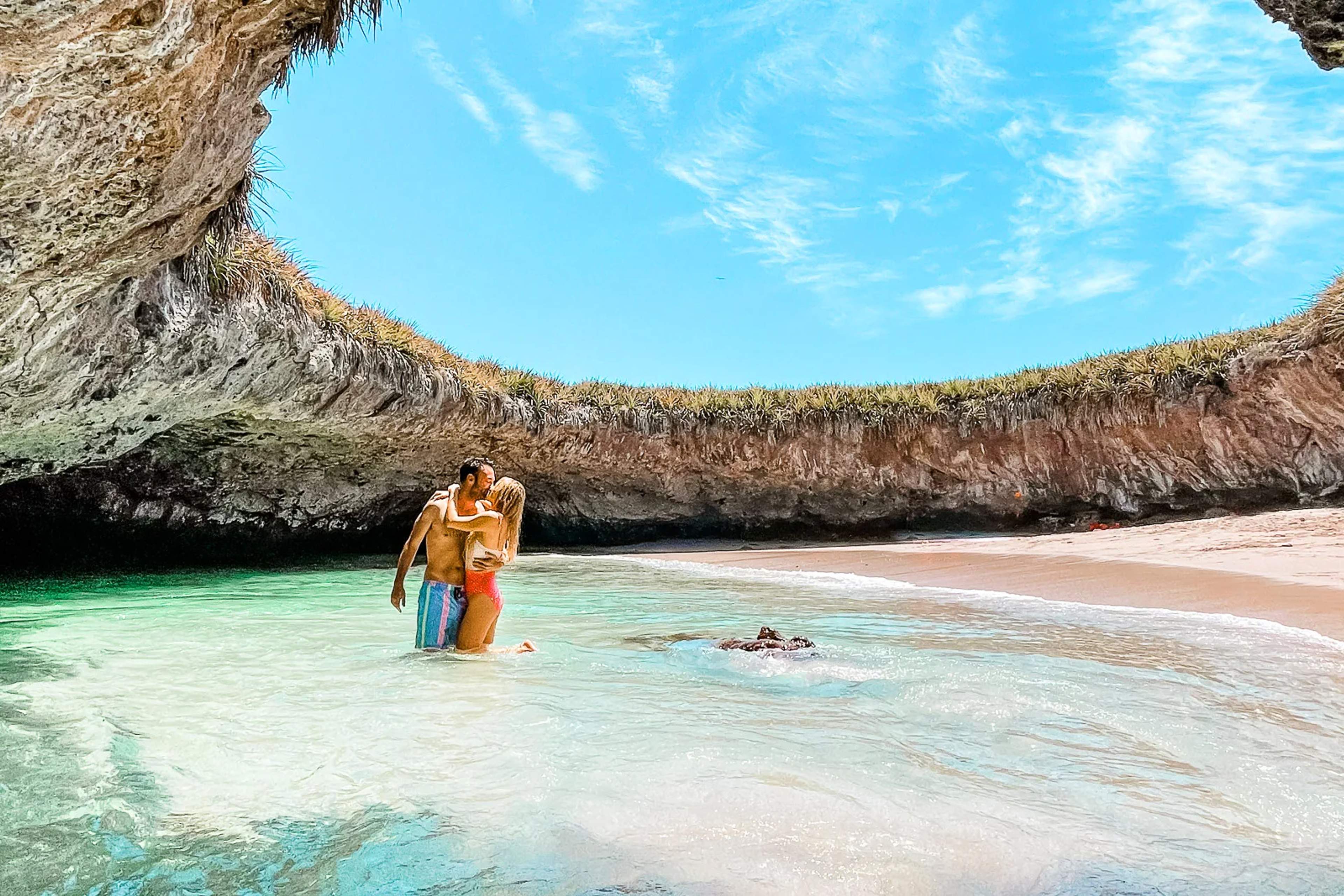 Un visitante camina por aguas cristalinas sosteniendo un flotador naranja cerca de la playa escondida en las Islas Marietas.