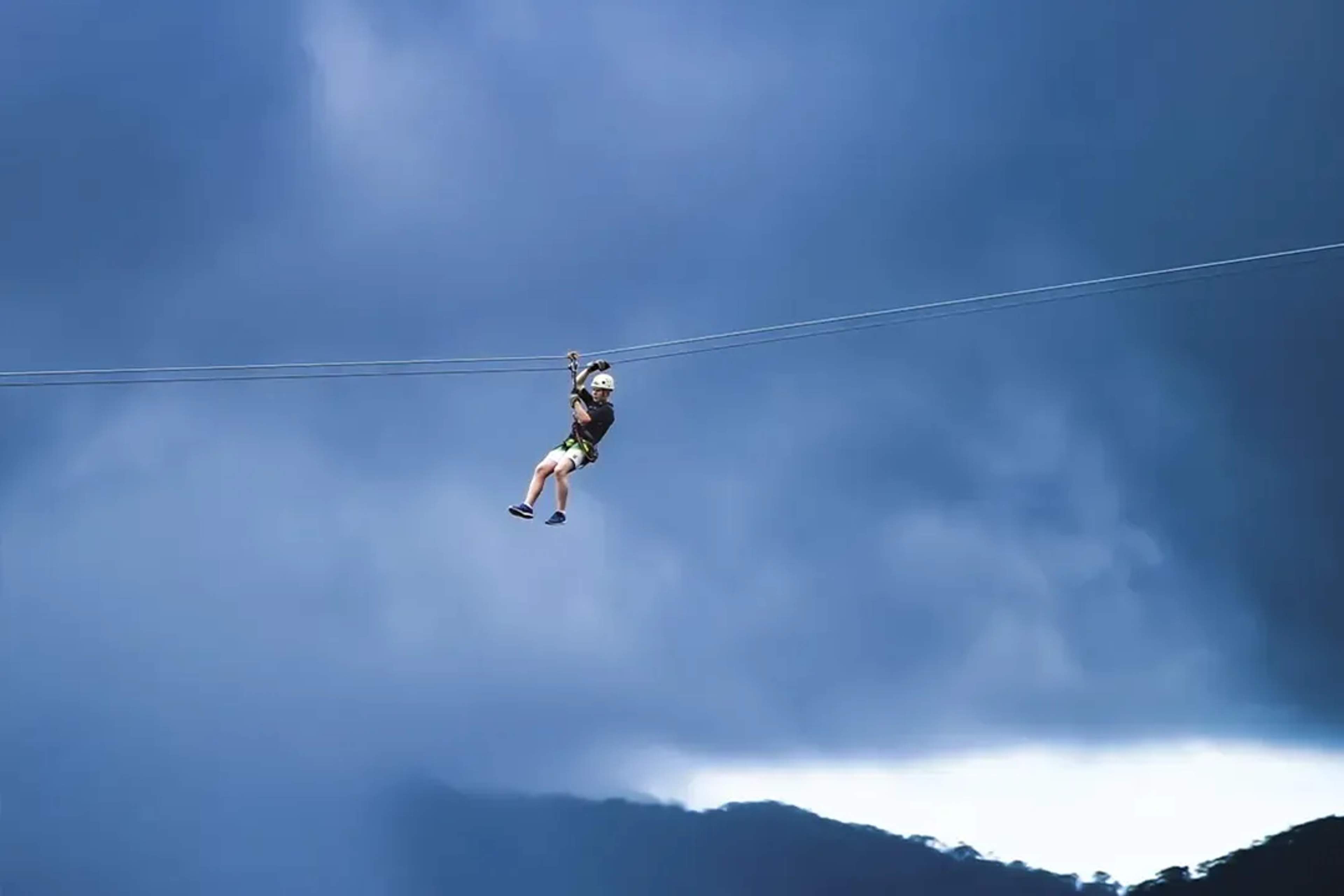 Persona en tirolesa vuela bajo nubes de tormenta en las montañas de Puerto Vallarta.