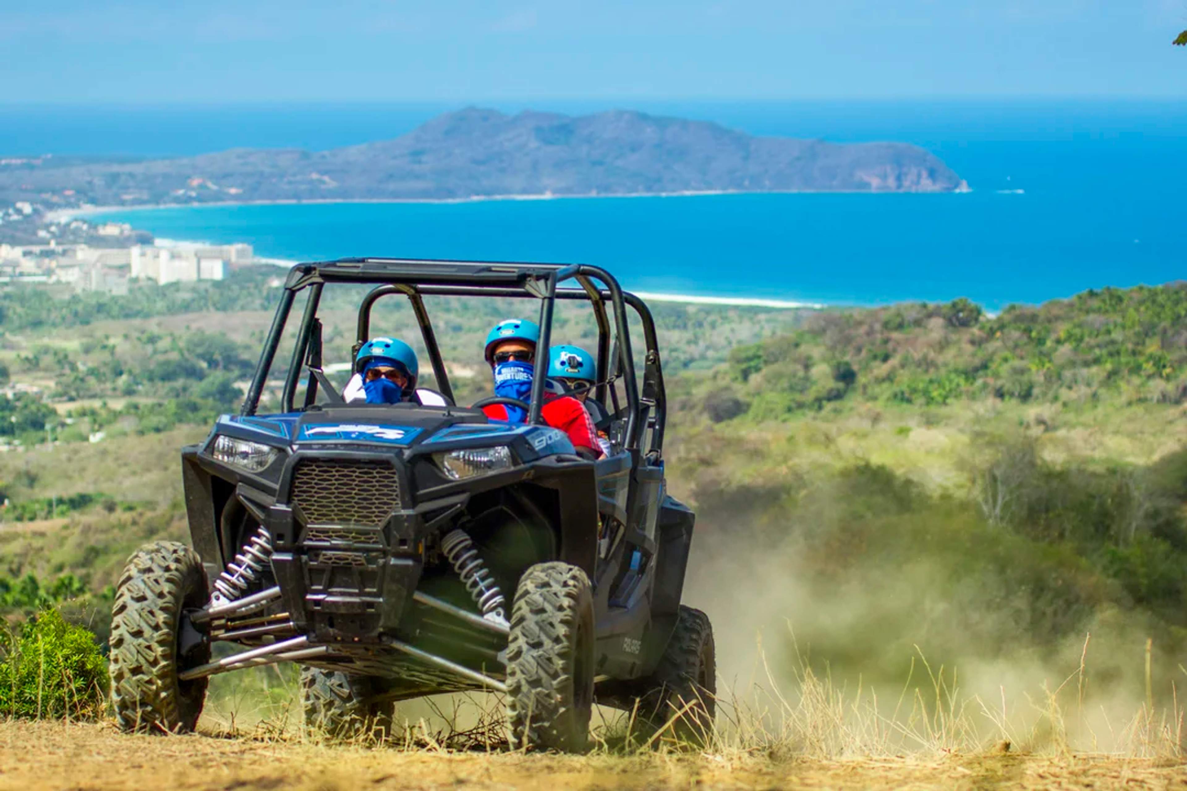 Adventurers ride a UTV through Sayulita's mountains, with ocean views and dust trails behind them.