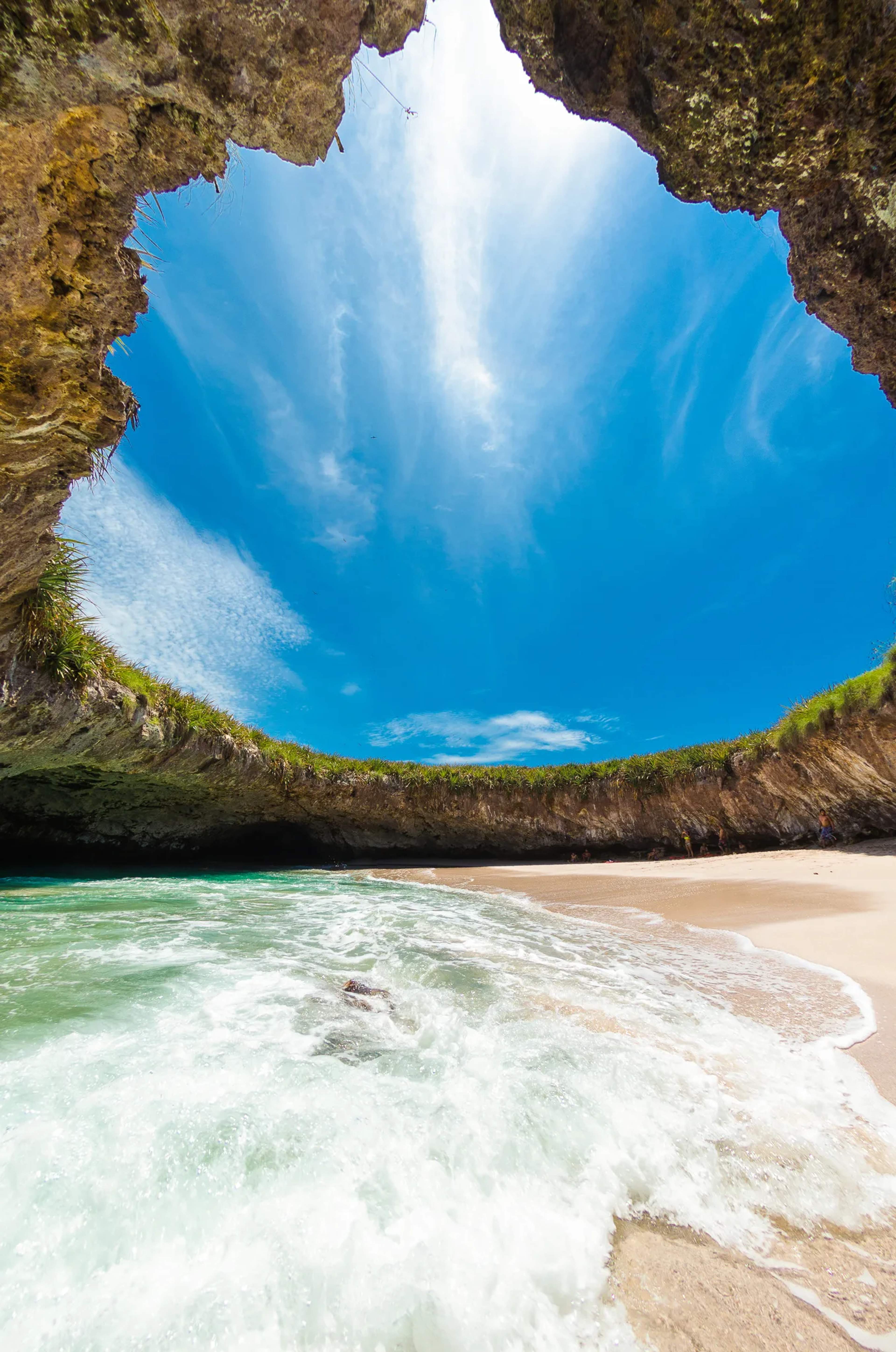 Hidden beach inside a dramatic rock cavern at Marietas Islands, with turquoise waves and white sand framed by towering stone